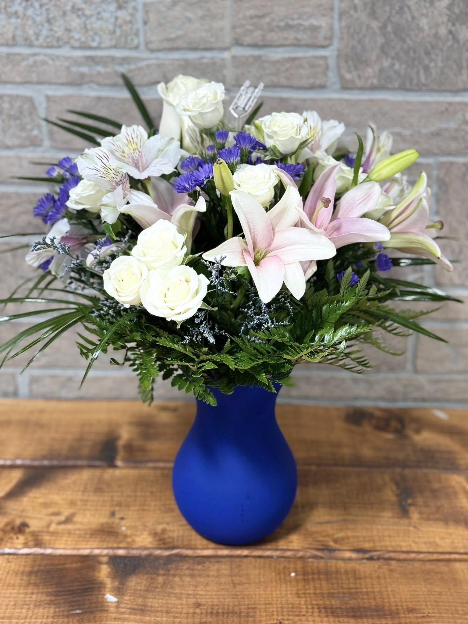 Grace in Bloom - Soft, elegant, and effortlessly beautiful—Grace in Bloom is a delicate expression of charm and serenity. Arranged in a calming blue vase, this bouquet features fragrant pink lilies, creamy white roses, soft white alstroemeria, accents of purple monte casino and limonium, and touches of robellini greenery. A perfect choice for expressing appreciation, sending gentle thoughts, or simply brightening someone's day with timeless elegance.