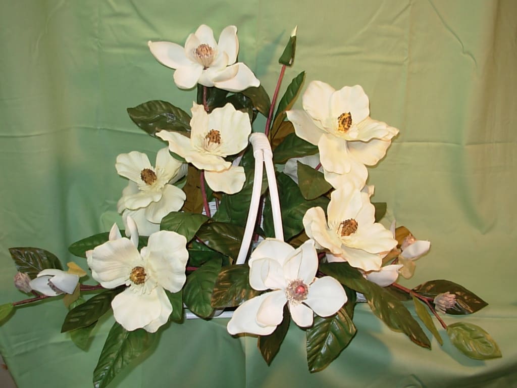 MAGNOLIA BASKET - SILK  NEW-S34 - Our silk-permanent MAGNOLIA FIRESIDE BASKET is an ideal expression  of love in remembrance of a lost love one.. White, silk -permanent southern magnolias arranged in a traditional wicker fireside basket is for the funeral service or for the family's home.. In the south traditionally set on the hearth. 