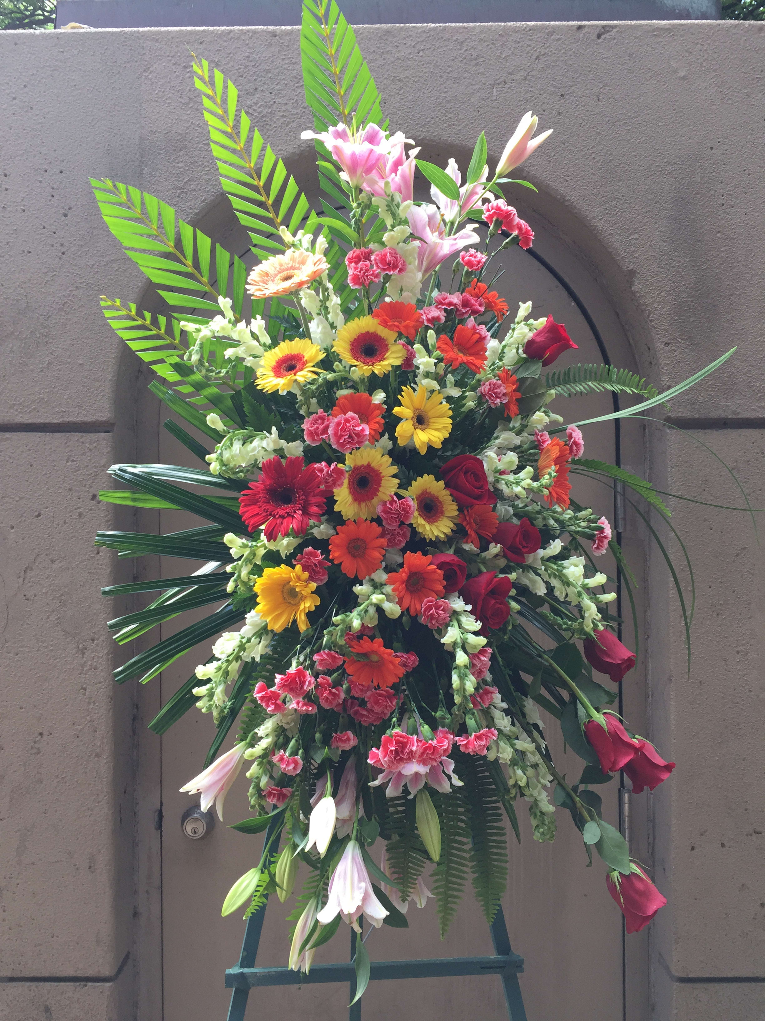 Mixed Spring Wreath - F020010 - Multi color flora for a cheerful look. This wreath consist of gerbera daisies, snap dragons, roses, lilies and carnations. Designer's choice of flowers when season available.