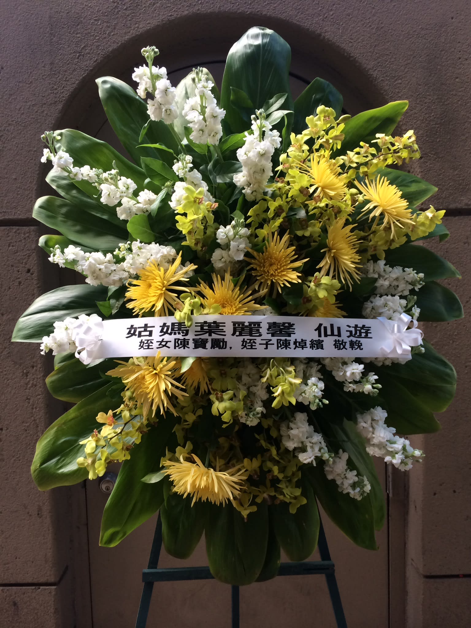 Yellow and White Theme Wreath - F175W03 Yellow and White Theme Wreath - F175W03 - Vibrant yellow chrysanthemum, spikes of light green orchids and sprays of stately white double stalks, surrounded by lush green ti leaves. Please inquire with designer for customization.