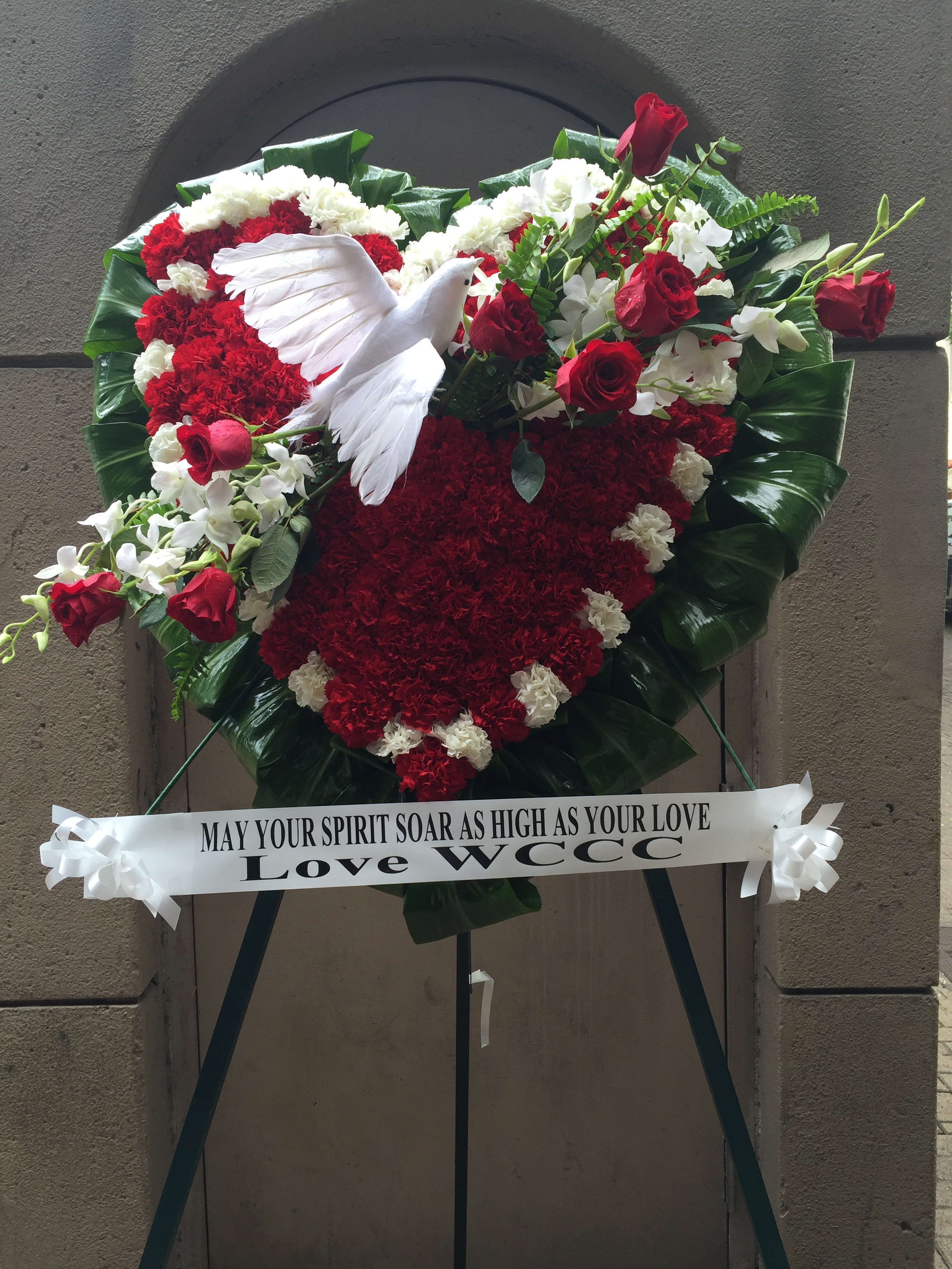 Wings of Grace - F35014 - Flying white Dove carrying beautiful red roses and orchids, soaring across a hear shape bed of red and white carnations surrounded with ti leaves. 