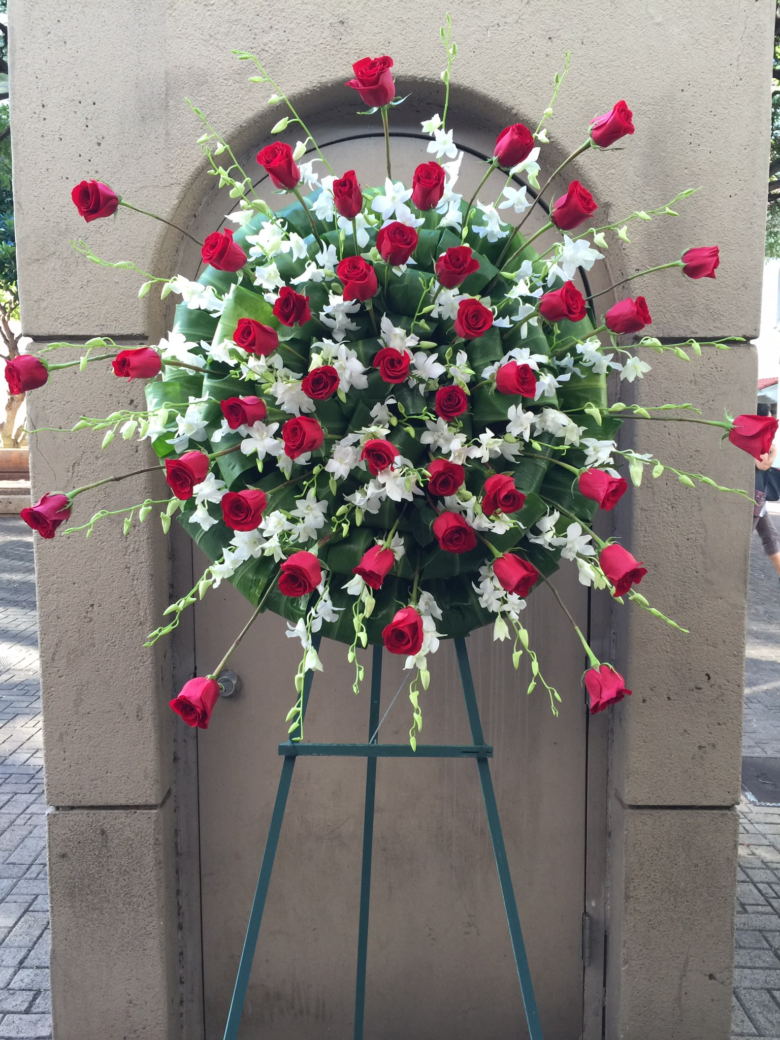 Sunburst red roses and sprays of white orchids wreath - F200W07 Sunburst red roses and sprays of white orchids wreath - F200W07 - Dramatic red and white sunburst theme of red roses and white orchids with ti leaves neatly tucked in a circular pattern background surround