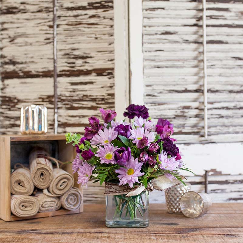 Shades of Purple by Barb's Flowers Shades of Purple by Barb's Flowers - This fun bouquet in shades of purple comes arranged in a clear square vase. Very stylish with Daisies, Alstromeria, Tulips or Roses & Carnations along with assorted greenery and fillers.