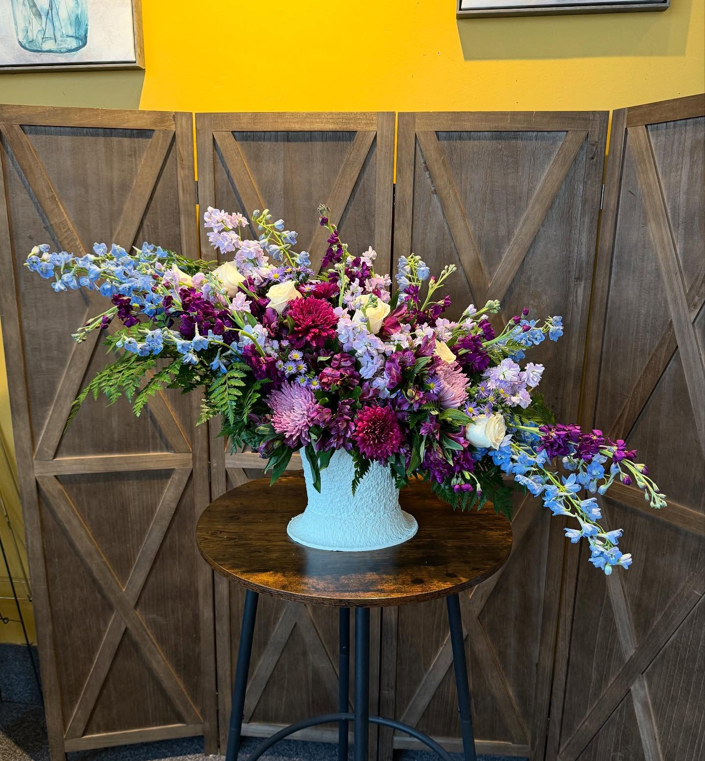 Purple Rain - &quot;Purple Rain&quot; is a breathtaking floral arrangement that evokes the serene beauty of a gentle rainstorm. Rich, deep purple blooms, including roses, mums, and delphinium take center stage, while soft lavender accents and subtle greenery add depth and texture. The design captures the delicate balance between bold color and graceful movement, with each flower seeming to sway like petals caught in a light, refreshing downpour. The soft contrast of the dark purples against the fresh green foliage creates an atmosphere of calm elegance, perfect for adding a touch of luxury to any setting.