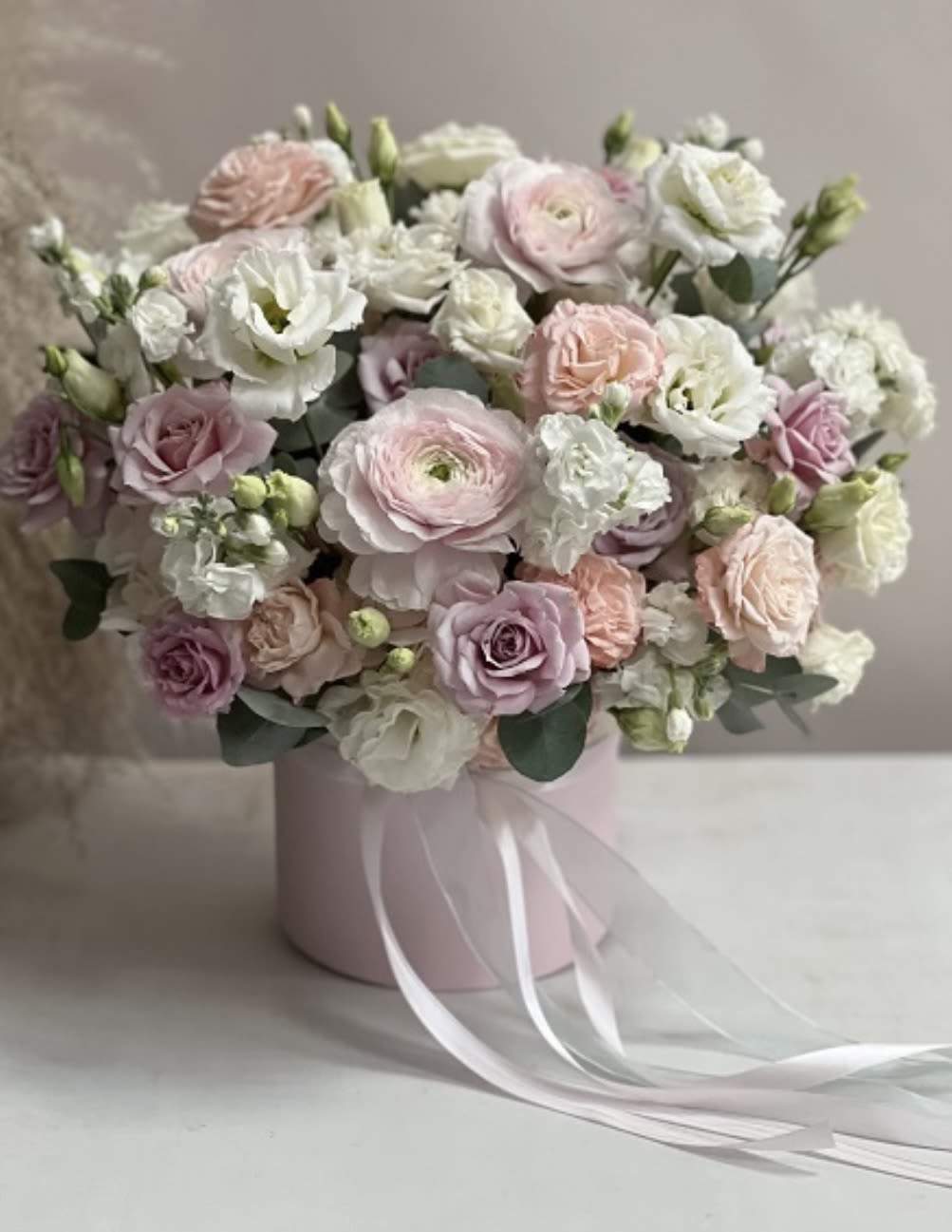Blush Whisper – Elegant Pastel Rose and Lisianthus - Delicate, dreamy, and full of poetic charm — this floral arrangement captures the timeless beauty of blush roses, white lisianthus, ranunculus, garden spray roses, and pale lavender blooms in a soft pink hatbox. Finished with flowing satin ribbons, it evokes quiet elegance and refined romance.  The airy pastel palette makes it an ideal choice for weddings, bridal showers, baby welcomes, anniversaries, or any occasion where gentle sophistication is desired. Each bloom is arranged to create a graceful balance of texture and tone, blending creamy whites, soft blush, and muted mauves into a harmonious composition.  Presented in a round box with trailing ribbon detail, this bouquet is both a luxurious gift and a beautiful decorative piece — perfect for the coffee table, entryway, or event display.  Same-day flower delivery available in Los Angeles.