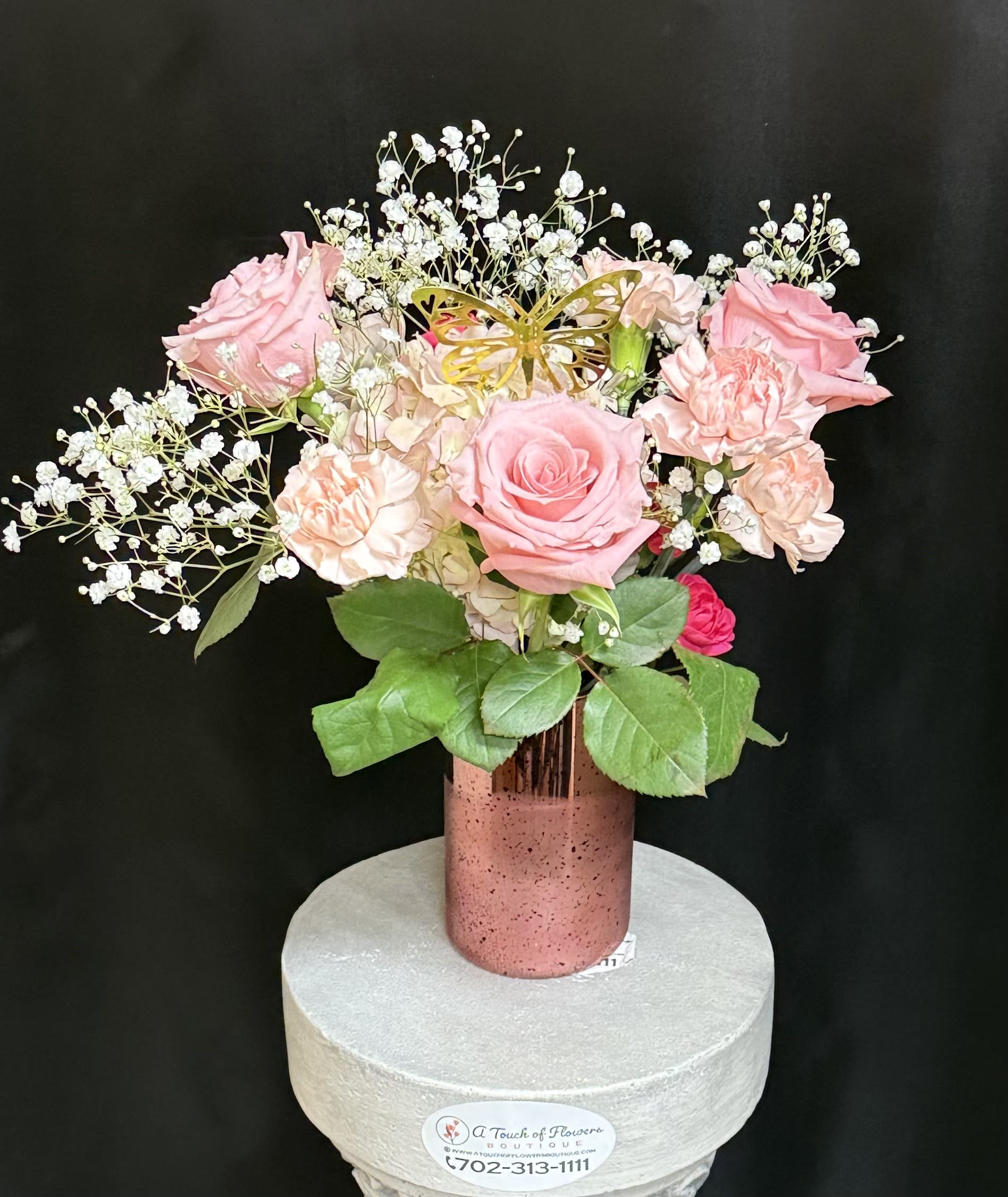 Butterfly Kisses  - Soft and sweet, and full of charm, butterfly Kisses is a delightful mix of blush pink roses, is a soft peach carnations, vibrant hot pink spray roses, and delicate baby's breath. Arranged in a shimmering rose gold vase and accented with a cheerful gold butterfly, this arrangement is a symbol of joy, transformation, and affection perfect for birthdays, get well wishes, or just because. 