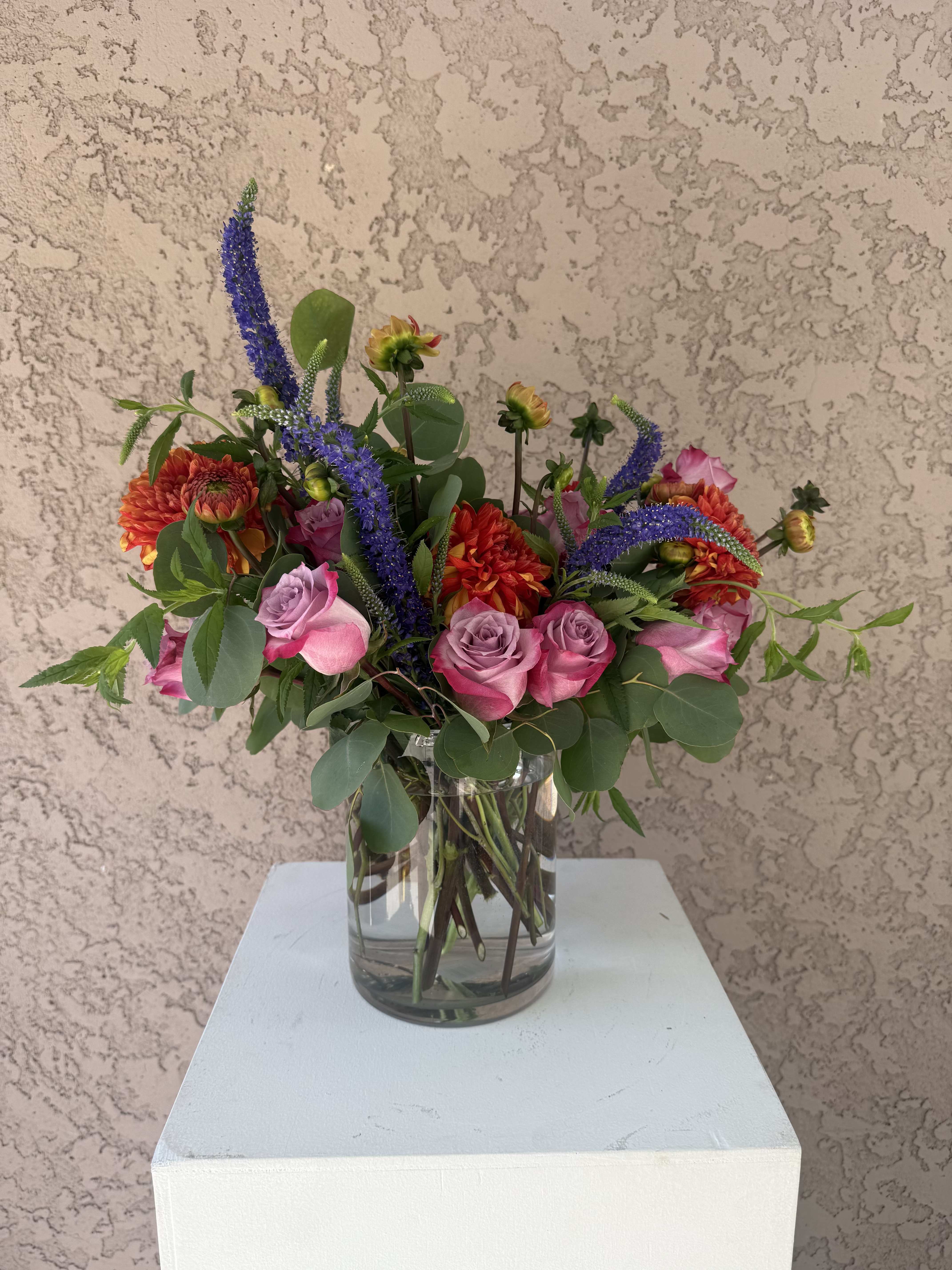 Wild Muse - Colorful, unexpected, and artfully arranged — Wild Muse is a free-spirited blend of lavender roses, fiery dahlias, blue veronica, and seasonal greens in a clear glass vase. Designed in Beverly Hills, CA and available for delivery across Los Angeles, this whimsical bouquet is perfect for birthdays, creatives, or anyone who appreciates wild beauty and bold expression. Handcrafted by Family Tree Flower, your trusted Beverly Hills florist offering luxury flowers and same-day delivery throughout LA.  Lavender Roses – Enchantment, love at first sight, elegance. Dahlias (orange/red) – Strength, creativity, dignity. Veronica (blue spires) – Fidelity, transformation, intuition.