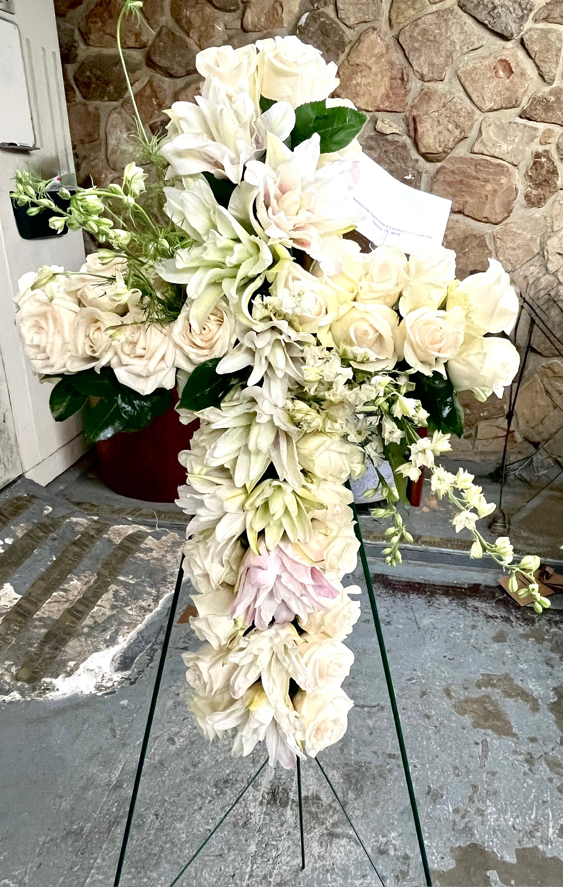 Forever Loved Sympathy Cross - White Standing Cross adorned with white Roses and Lilies for the loveliest of celebrations. Send your heartfelt condolences with memories to last a lifetime with this classic timeless piece. For the home or service.  Stands on a 54&quot; Easel