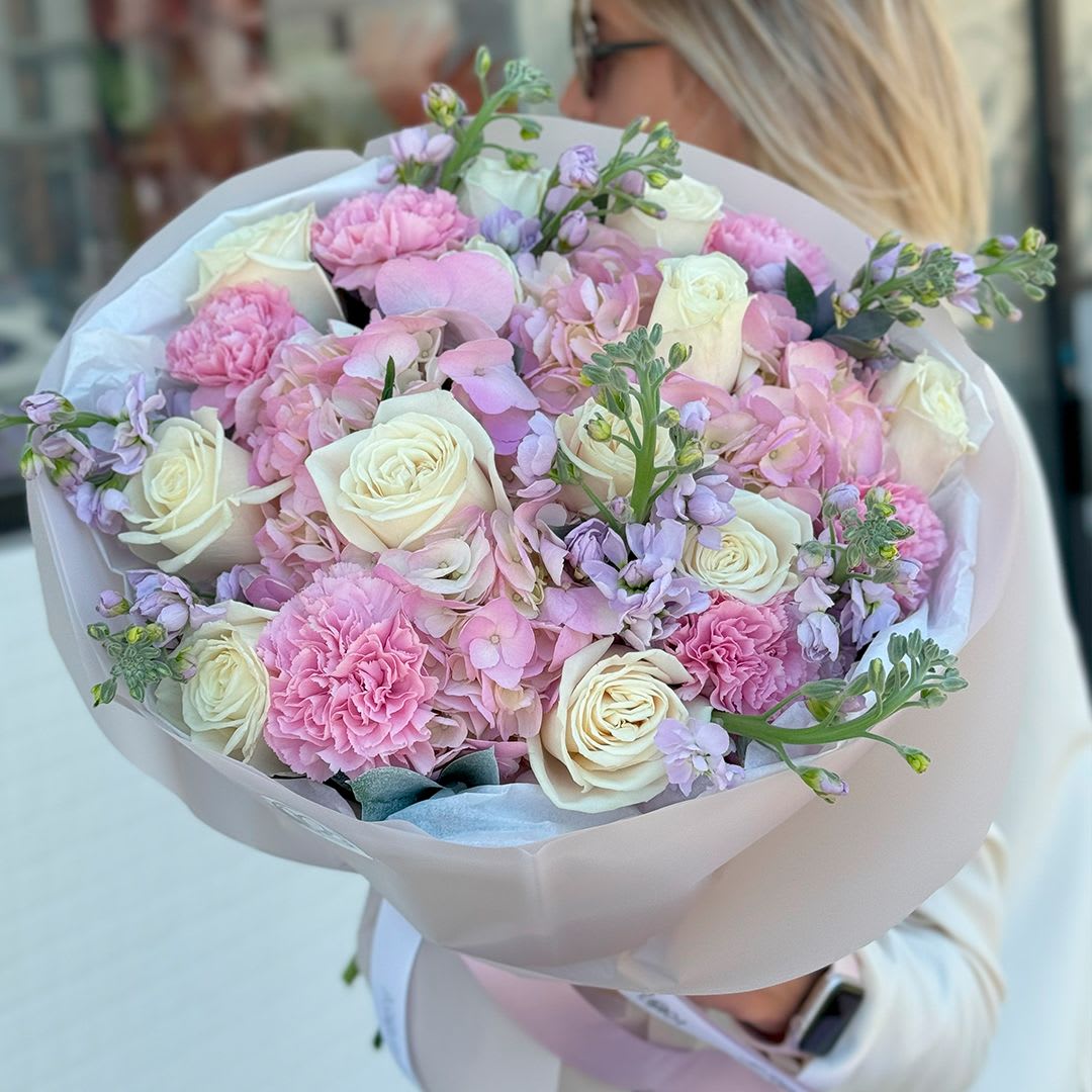 Blossom Symphony - A tender and romantic composition, Blossom Symphony enchants with its soft palette of creamy white, delicate blush pink, and pastel lavender. This bouquet features elegant white roses, lush pink carnations, dreamy pink hydrangeas, and whimsical lilac matthiola. Wrapped in soft pearl paper with a satin ribbon, it’s a perfect gift to express gratitude, admiration, or love. Ideal for birthdays, anniversaries, or simply to brighten someone’s day with floral elegance.