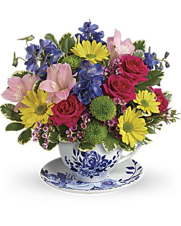 Dutch Garden Bouquet  - Inspired by classic Delft pottery, this downright delightful glazed ceramic teacup and saucer is a whimsical way to surprise them with a joyful bouquet of roses, alstroemeria and delphinium! Hot pink spray roses, light pink alstroemeria, blue delphinium, green button spray chrysanthemums and yellow daisy spray chrysanthemums are accented with lavender waxflower and variegated pittosporum. Delivered in a Dutch Garden teacup. Arrangement is considered small. 