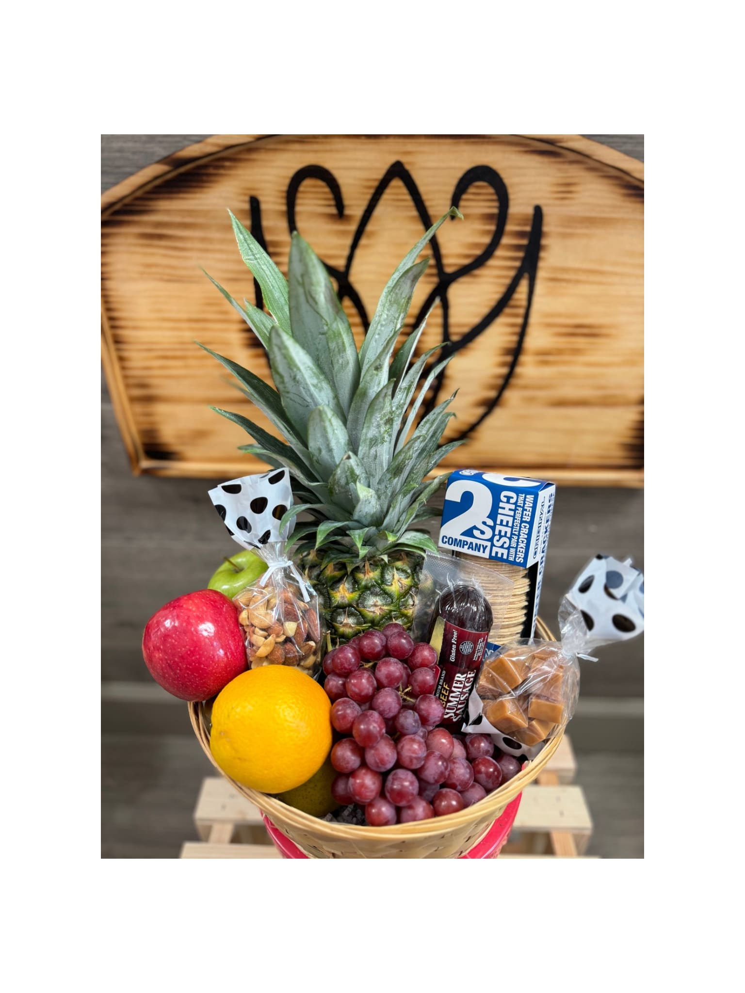 Nourish Nest Basket - Brighten someone’s day with vibrant basket of fresh, seasonal fruit- perfect as a get-well or a thoughtful gesture.  .Apples, pears, oranges, grapes, and a pineapple are presented with crackers, sausage and other savory snacks in a natural gift basket that's wrapped and trimmed with a bow.