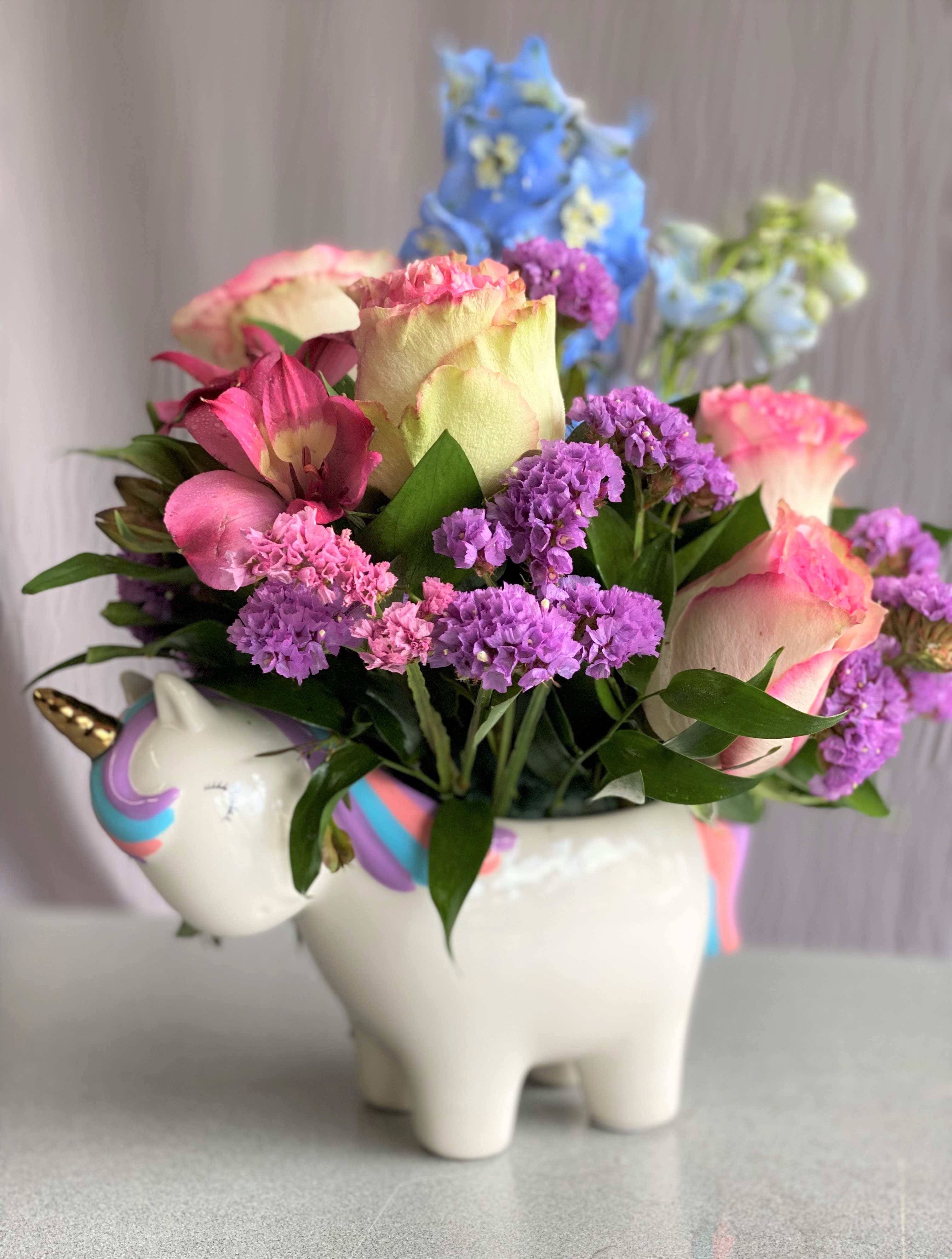 SWEET UNICORN - Make magic with this joyful gift with a mix of roses, delicately arranged in this sweet ceramic unicorn keepsake that's hand-painted for an extra-special touch! Roses, Spray Roses, White Alstroemeria, miniature carnations, blue sinuata statice, and pink waxflower are accented with pitta negra. Orientation: All-Around