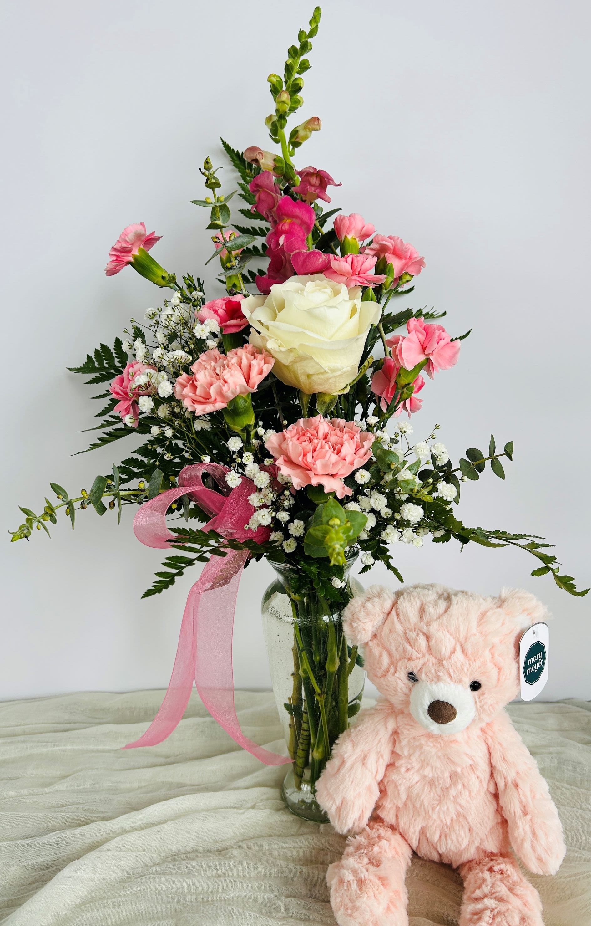 It's a Girl - Gift Set!  - This adorable arrangement consists of a white rose, pink carnations, pink mini-carnations, a bright pink snapdragon, and is styled in a vase with baby's breath, greens, and a pink bow.  