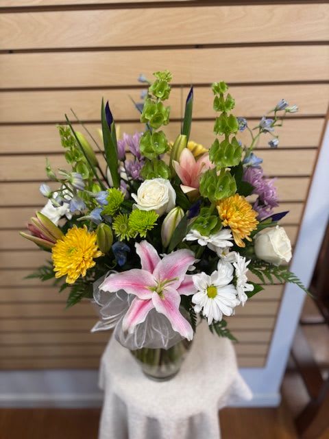 Soft Goodness - Mixed cut arrangement with white roses, yellow mums, bells of ireland, white daisies, lavender cushions, blue delphinium and stargazer lilies in a vase with a bow