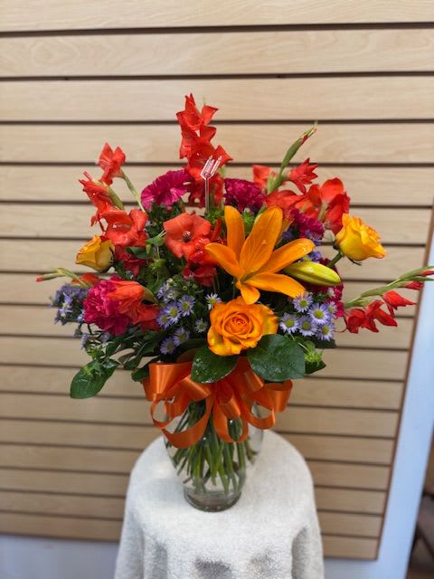 Ruby  - Mixed cut arrangement with red glades, orange lilies, circus rose, lavender accent, and hot pink carnations in a vase with a bow