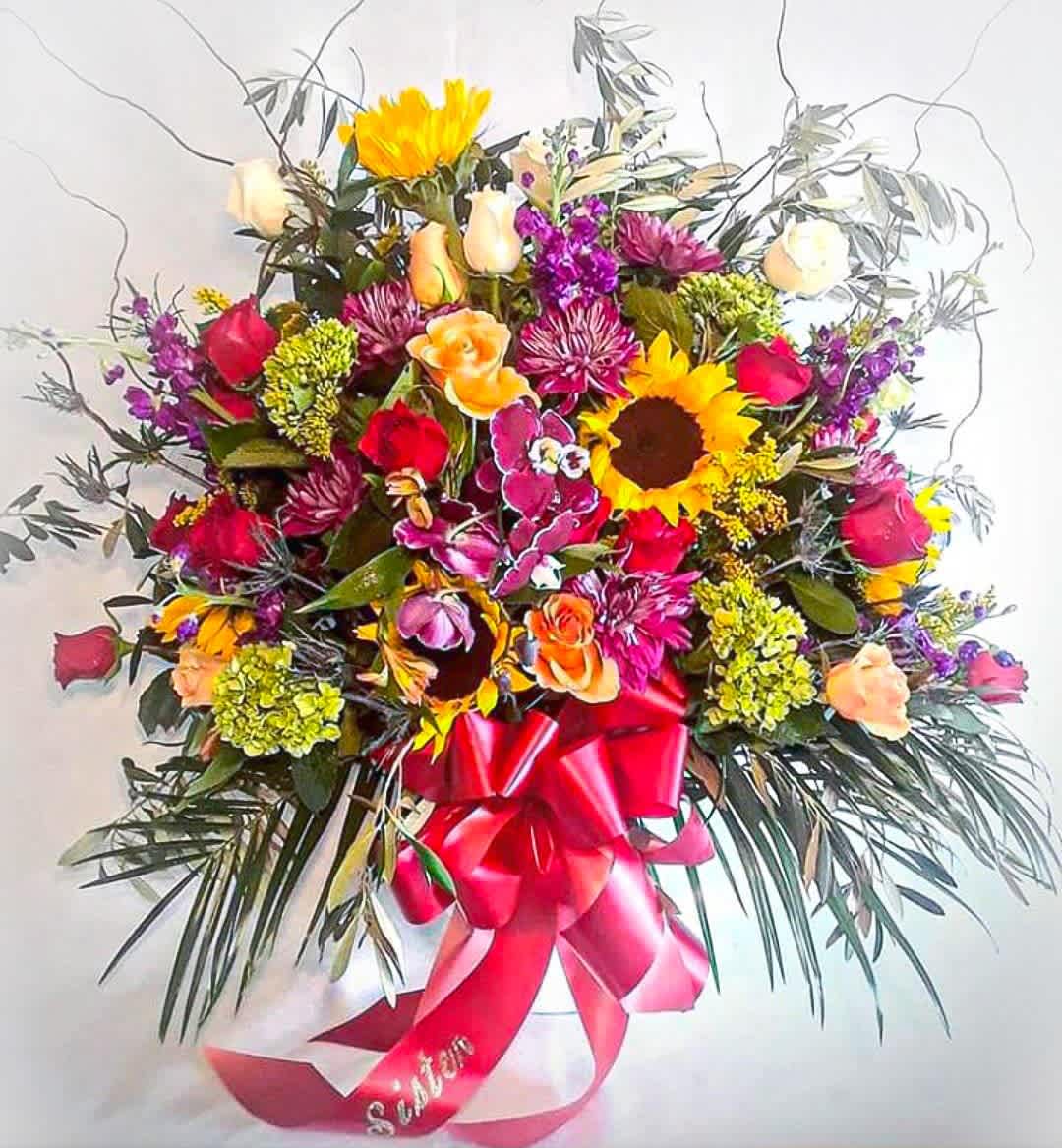 Autumn Sympathy Spray - Send this beautiful spray today to show them how much you care with it's lovely fall mixed blossoms of the day roses orchids sunflowers and more arranged in a modern white vessel vase perfect to send to the service. Always made extra special and unique each time. Send them your deepest condolences.