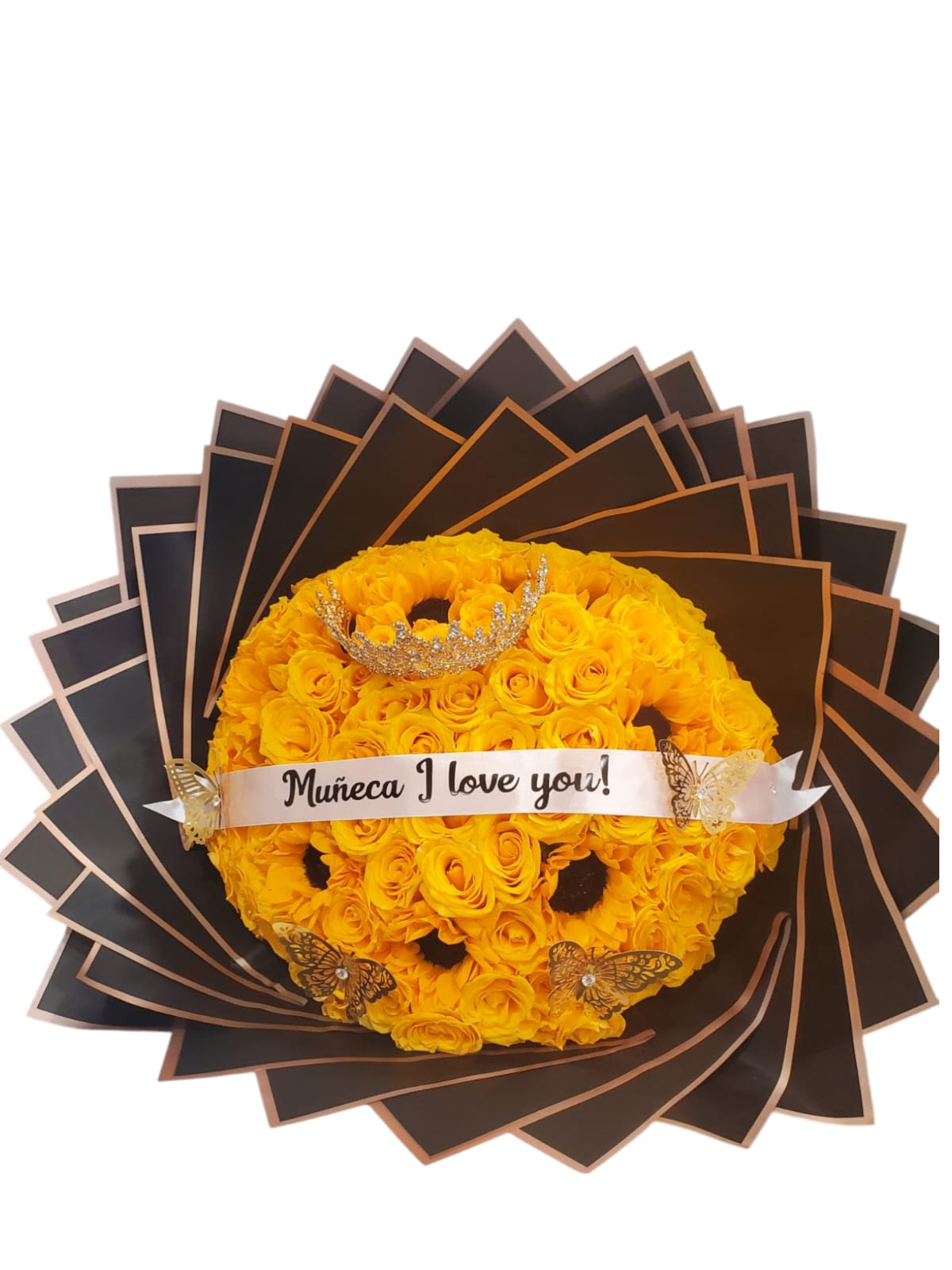 Reina de Sol - Este arreglo floral es una expresión de amor y cariño a través de la combinación de la belleza clásica de los girasoles y rosas, el toque de lujo de la corona y las mariposas, y el mensaje  en la cinta.