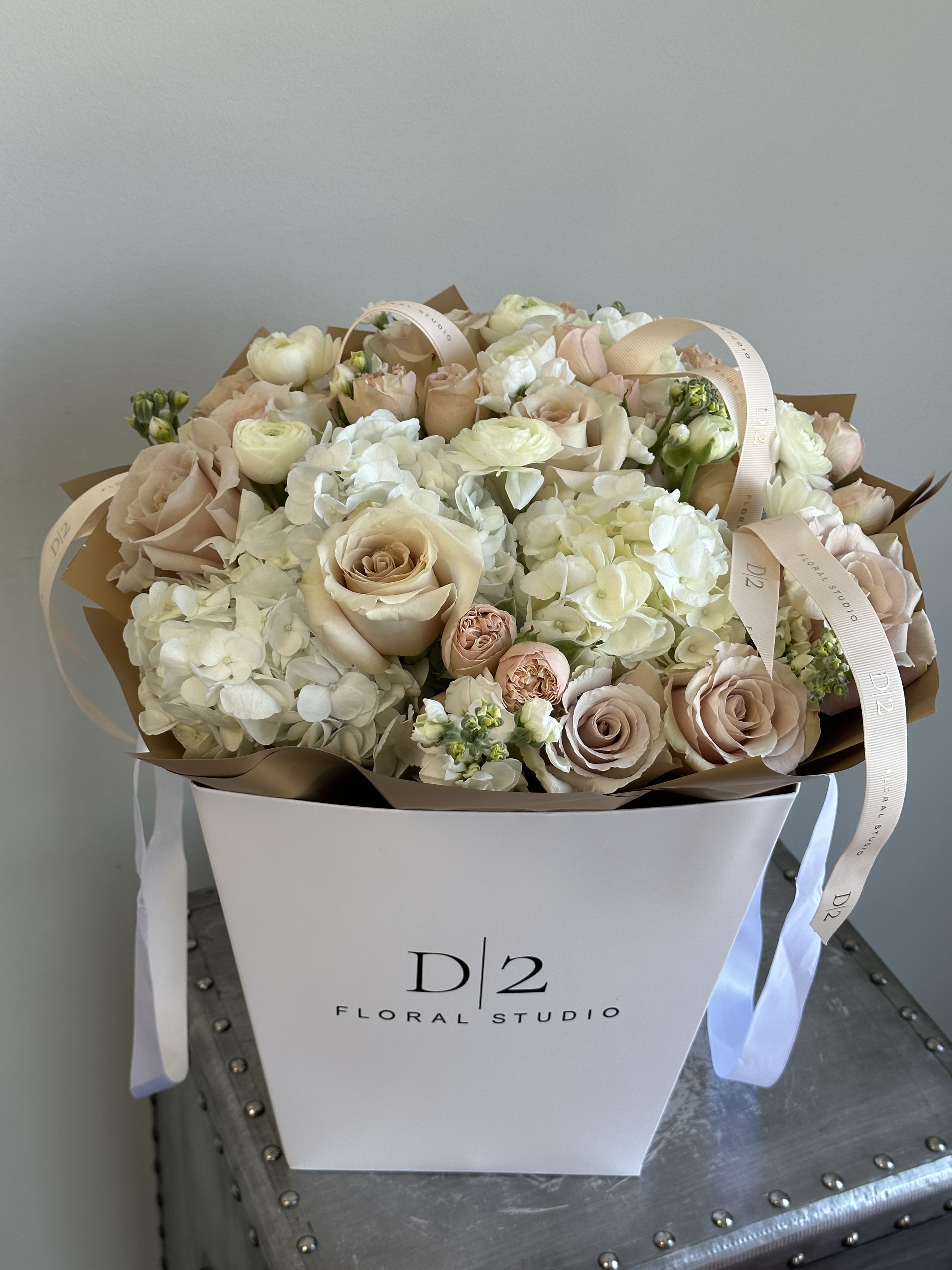 June - A chic and modern floral arrangement presented in a signature D|2 Floral Studio bag, featuring a soft palette of cream, blush, and nude roses paired with lush white hydrangeas and delicate filler blooms—perfect for elegant gifting or luxury celebrations.