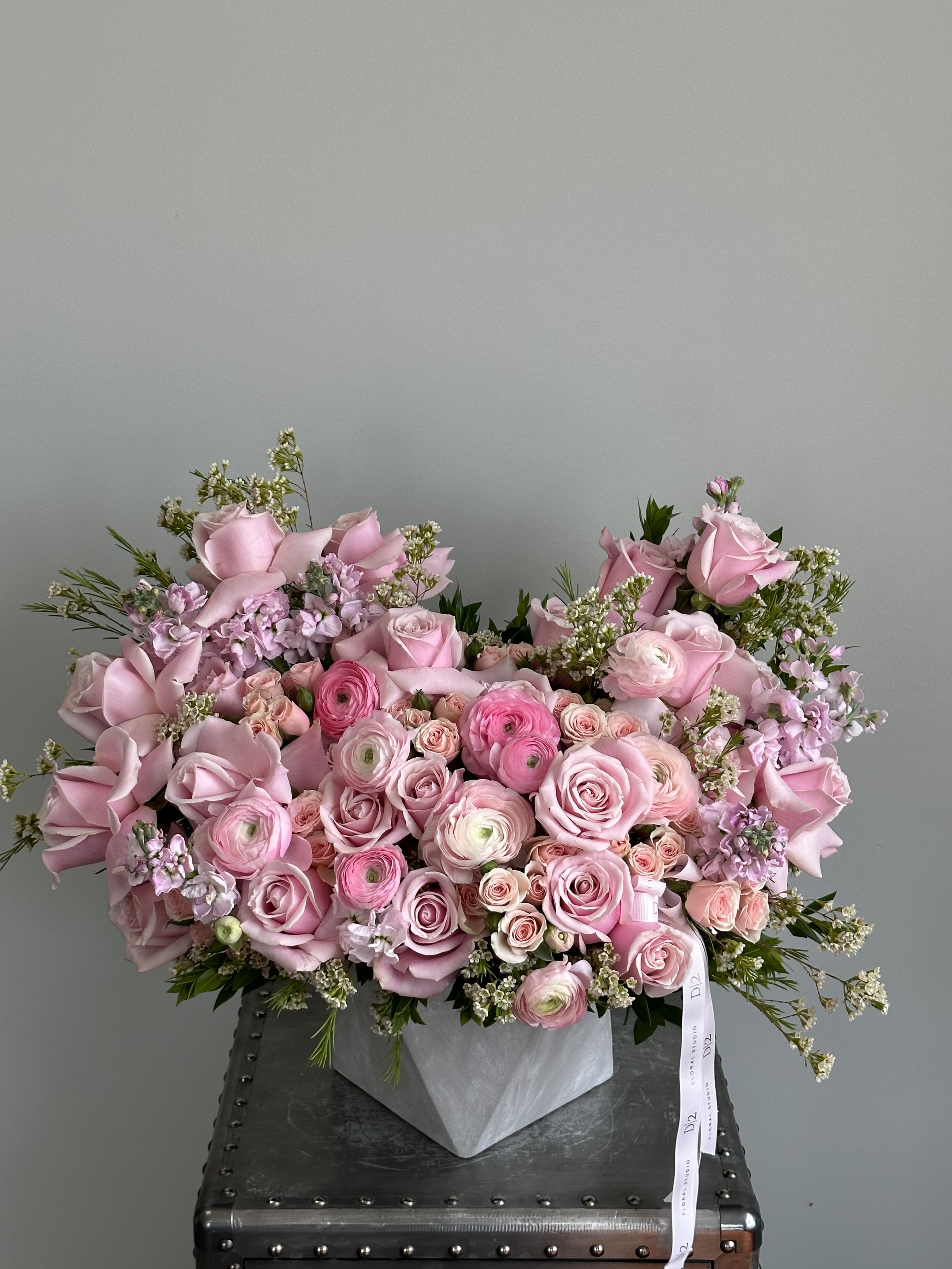 Valeria - A lush and cheerful arrangement bursting with shades of pink, featuring roses, ranunculus, spray roses, and delicate fillers, artfully styled in a modern geometric vase and finished with a soft ribbon—perfect for birthdays, anniversaries, or joyful celebrations.