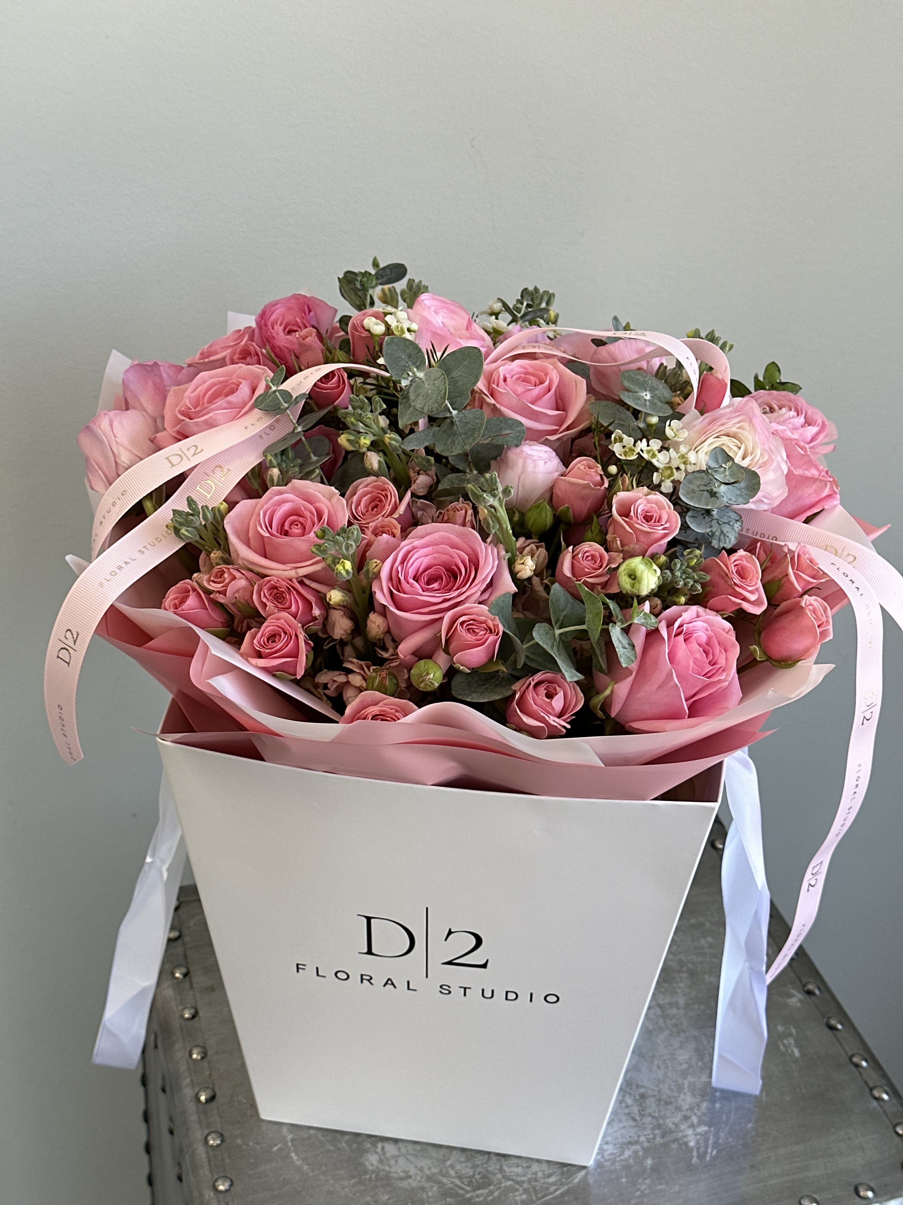 Isabel - A vibrant and playful arrangement of hot pink roses, spray roses, ranunculus, and touches of eucalyptus, stylishly wrapped in soft pink paper and presented in a signature D|2 Floral Studio gift bag—perfect for birthdays, celebrations, or a bold romantic gesture.