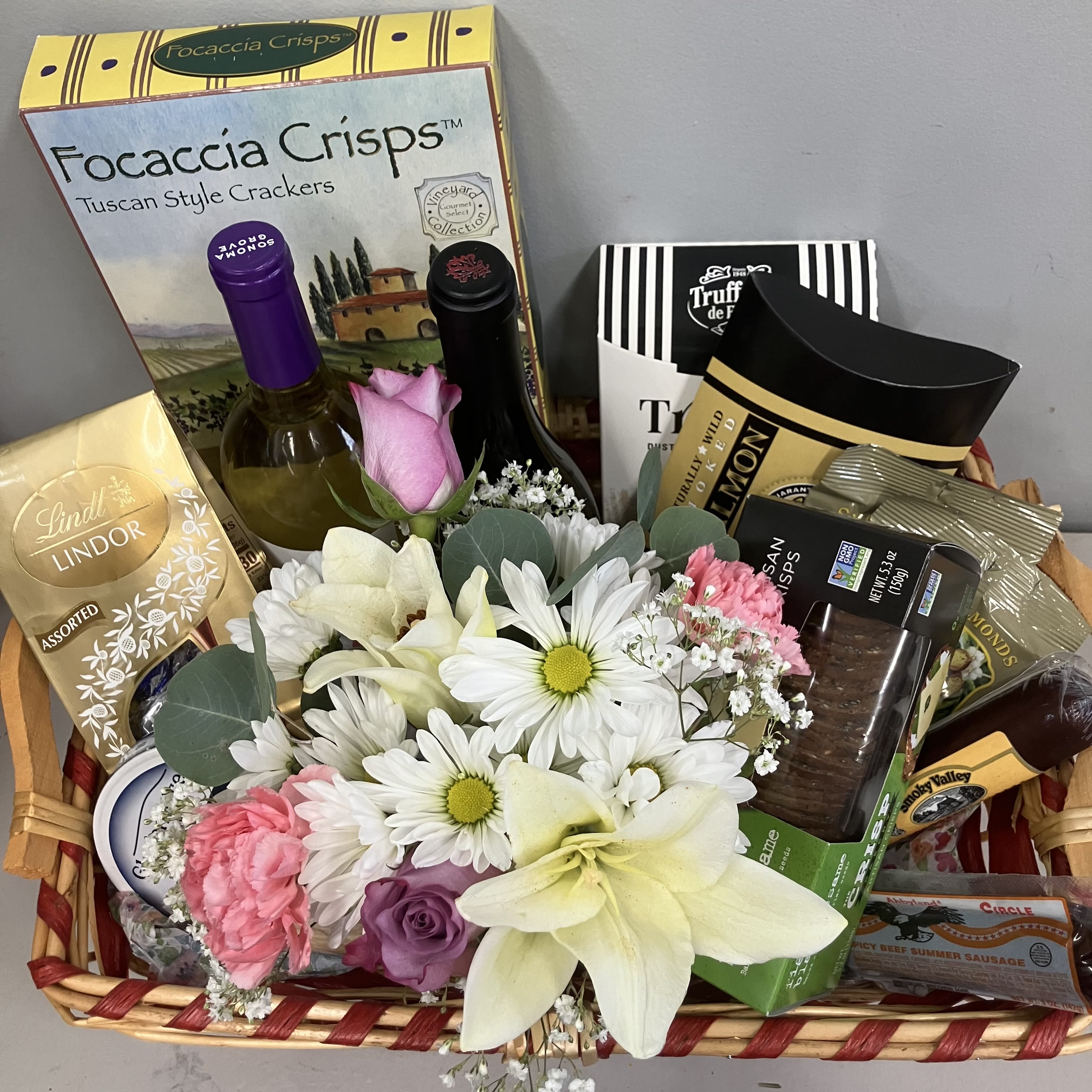 Wine and Snack Gift Basket - Send an outstanding gift basket that includes, two bottles of wine, two cheese options, two meats, salted almonds, crackers, truffles, and a sweet flower arrangement of white daisies and purple roses. Beautiful gift for many occasions 