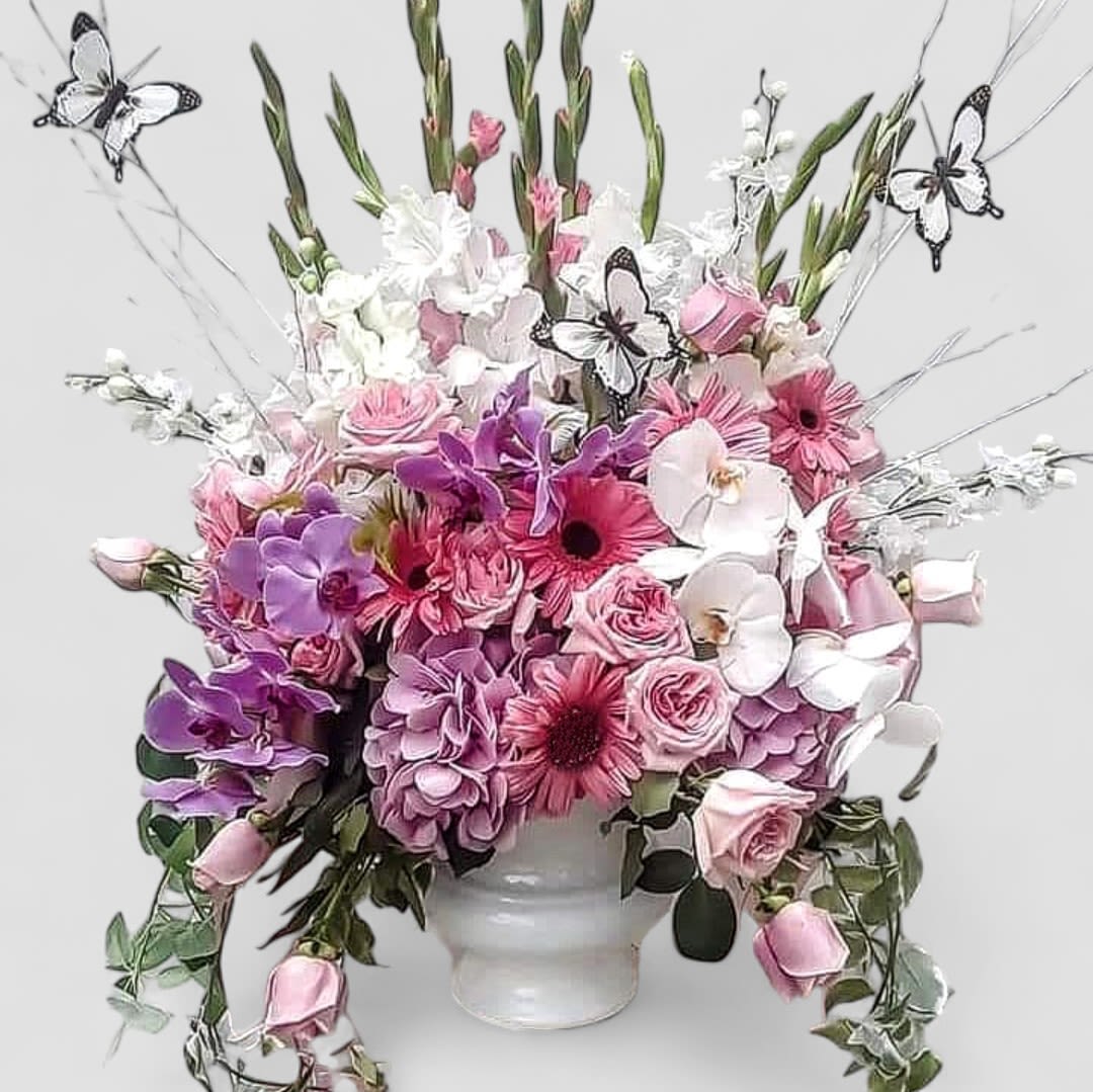 Pink And White Butterfly Sympathy Spray - Send this beautiful elegant tall sympathy arrangement today to show them how much you care with it's lovely mixed pink and white blossoms of the day roses orchids hydrangeas daisies and more arranged in a tall modern white vessel vase adorned with butterflies. Grand and spectacular to help celebrate a life well lived. Always made extra special and unique each time. Send them your deepest sympathies.