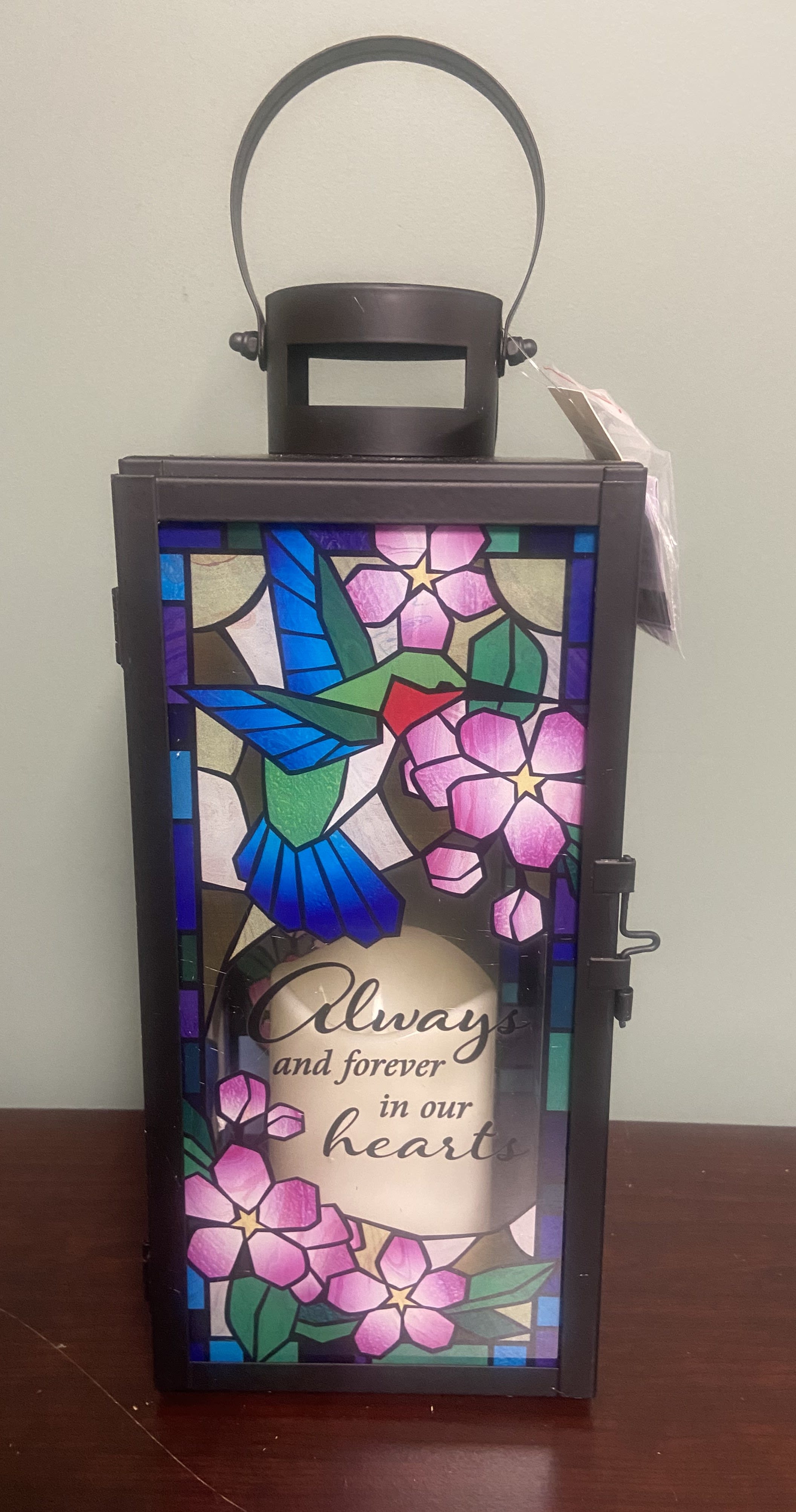 &quot;Stained Glass&quot; Lantern - This beautiful lantern has a flameless LED candle, it is made of a high quality black metal and a colorful stained glass effect on the pane;s.  Amidst the bird and flowers it reads &quot;Always and forever in our hearts&quot;  Item is 14&quot;H x 5&quot;W x 5&quot; D.  
