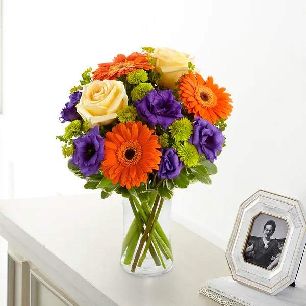 Rays of Solace Bouquet - Our Rays of Solace Bouquet is a cheerful burst of color to extend your deepest sympathies. Crème de la Crème roses, orange gerbera daisies, purple lisianthus, green button poms and a mix of vibrant greens are beautifully arranged in a clear glass gathering vase to create a warm bouquet expressing hope with every colorful bloom. 
