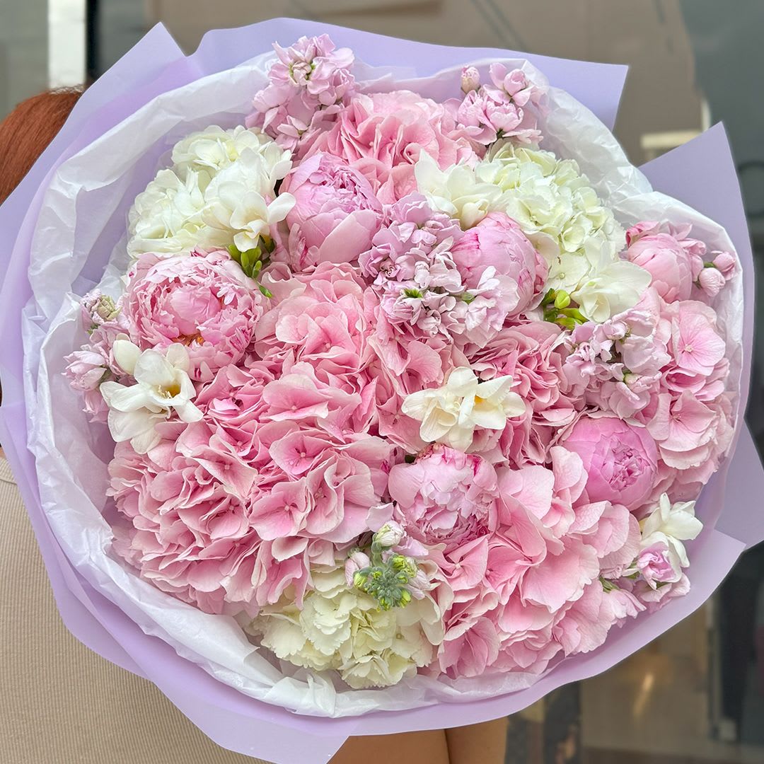 Pink Cloud - A delicate and voluminous bouquet that feels like a dream. Soft pink hydrangeas, romantic peonies, airy lisianthus, and creamy white blooms come together in a luxurious cloud of pastel beauty. Wrapped in lilac paper with a satin ribbon, this arrangement is perfect for celebrating love, femininity, and unforgettable moments.