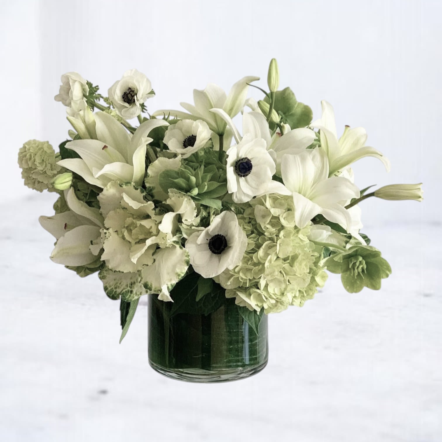 Verdant Tranquility - Verdant Tranquility is a peaceful blend of white lilies, ivory anemones, soft hydrangeas, and green accents — designed to evoke healing, balance, and calm. Artfully arranged in a clear glass cylinder with modern greenery, this bouquet is perfect for sending recovery wishes, hospital cheer, or a breath of fresh air after surgery.  Hand-delivered throughout Houston and surrounding areas with same-day availability, this green and white floral arrangement is ideal for get well occasions, sympathy gestures, or minimalist home decor.