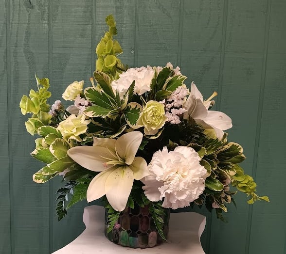Green Mosaic Green Mosaic - Elegant and serene, our "Green Mosaic" arrangement features striking Bells of Ireland, fragrant white Asiatic lilies, classic white carnations, green mini carnations, and delicate white statice. Designed in a stunning green stained-glass mosaic cylinder and accented with rich pittosporum and baker fern, this arrangement radiates natural beauty and tranquility—perfect for any occasion that calls for a touch of refined charm. Upgrading to Deluxe or Premium will include elegant white roses for an elevated look.