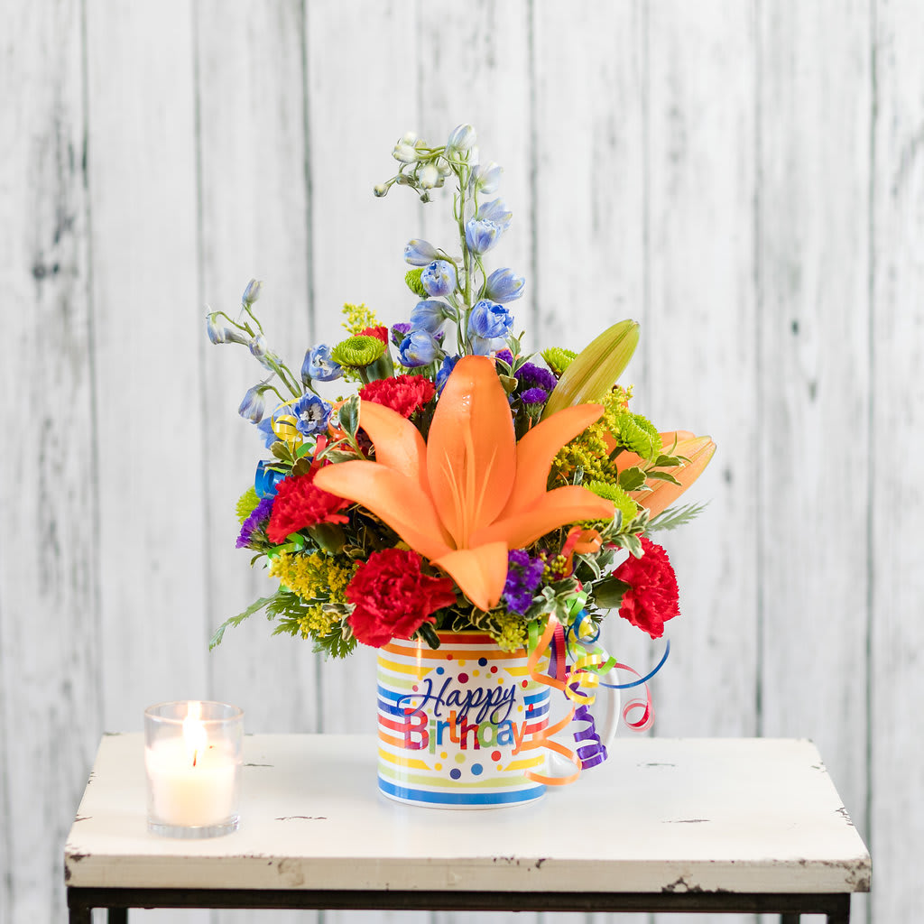 Surprise - Celebrate with a bright birthday arrangement in a reusable mug!  Colored streamers add a festive accent!  Approximate Dimensions: 9&quot; W x 14&quot; H