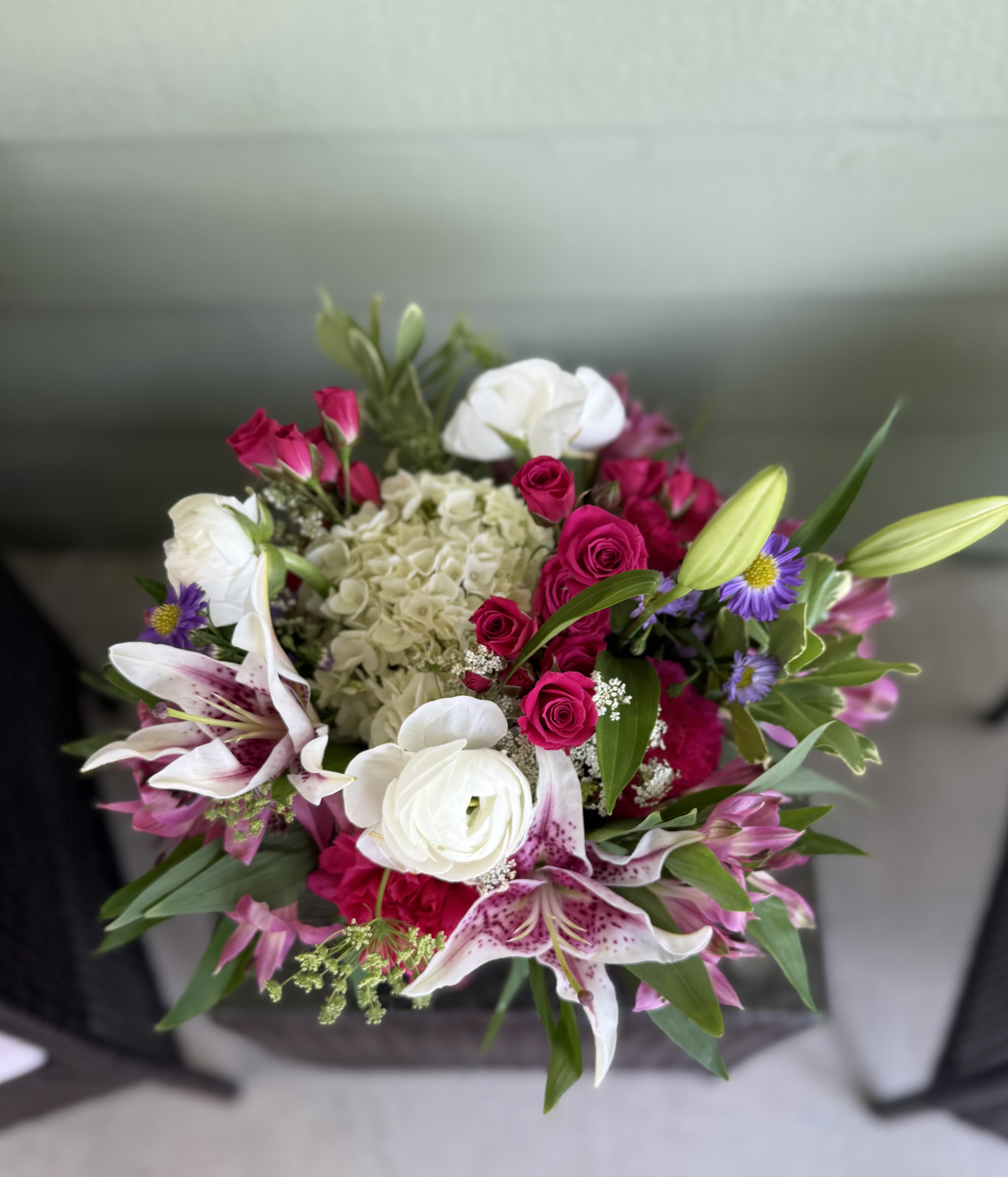Blushing Radiance – Premium Mixed Bouquet - Overflowing with vibrant charm, our Blushing Radiance arrangement is a joyful expression of beauty and elegance. Featuring fragrant Stargazer lilies, hot pink spray roses, white ranunculus, classic hydrangeas, and delicate accent blooms like alstroemeria and purple asters, this bouquet bursts with color and personality. Nestled in a clear glass vase, it’s the perfect gift for birthdays, anniversaries, congratulations, or just because.  Each bloom is carefully selected to create a harmonious blend of bold hues and soft textures – a stunning centerpiece for any occasion.