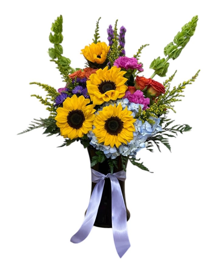 Vibrant Sunburst - This vibrant bouquet features cheerful sunflowers with their bright yellow petals and dark centers, complemented by soft, creamy yellow carnations and delicate snapdragons in shades of pale yellow. Lush green foliage adds fullness and contrast, creating an arrangement that radiates warmth and sunshine. Perfect for brightening any space or celebrating joyful moments, this lively floral display embodies the spirit of happiness and vitality.