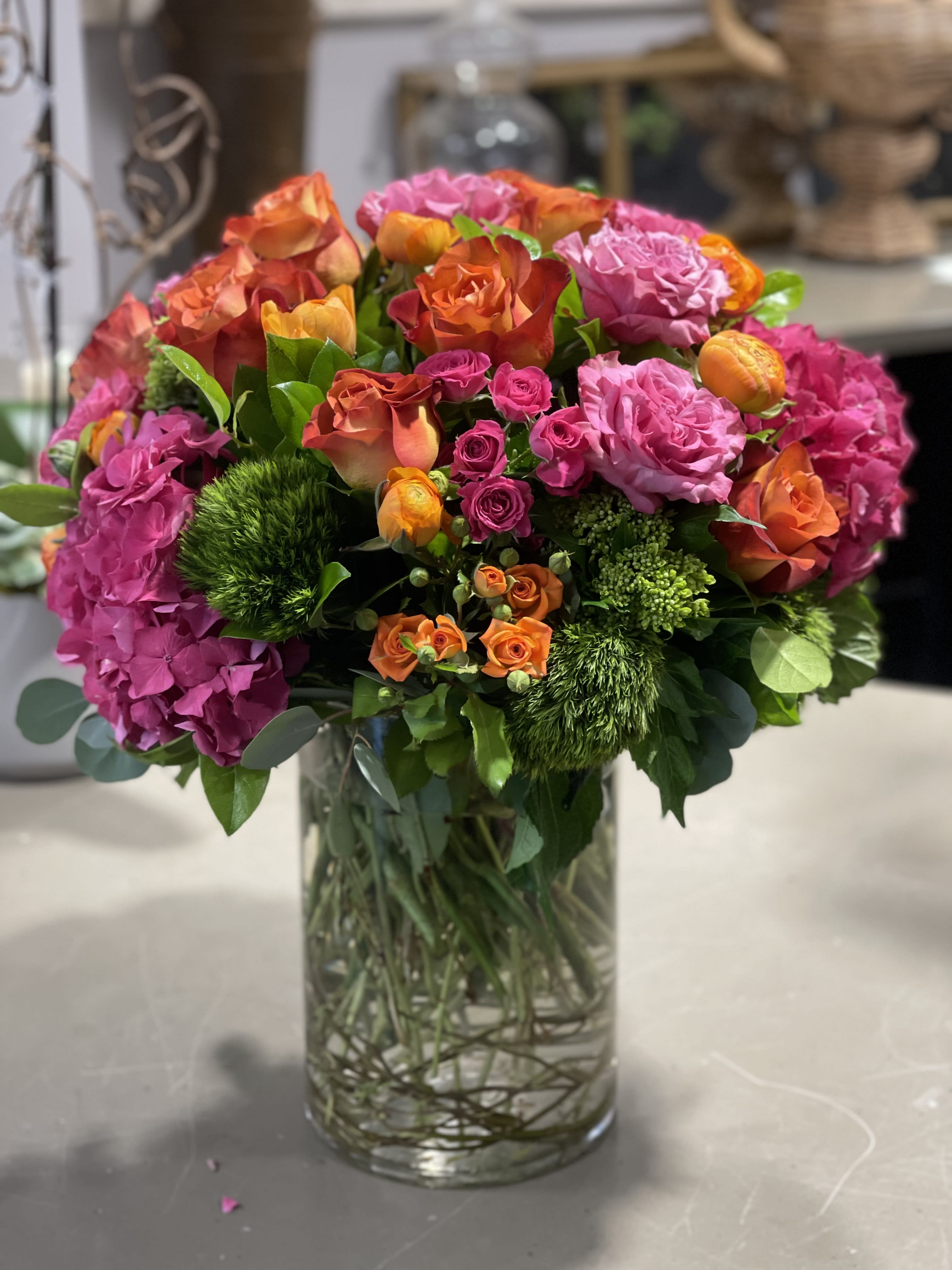 Radiance - A Beautiful combination of Hydrangeas, Roses, Spray Roses, Dianthus and other seasonal flowers in a tall glass cylinder vase