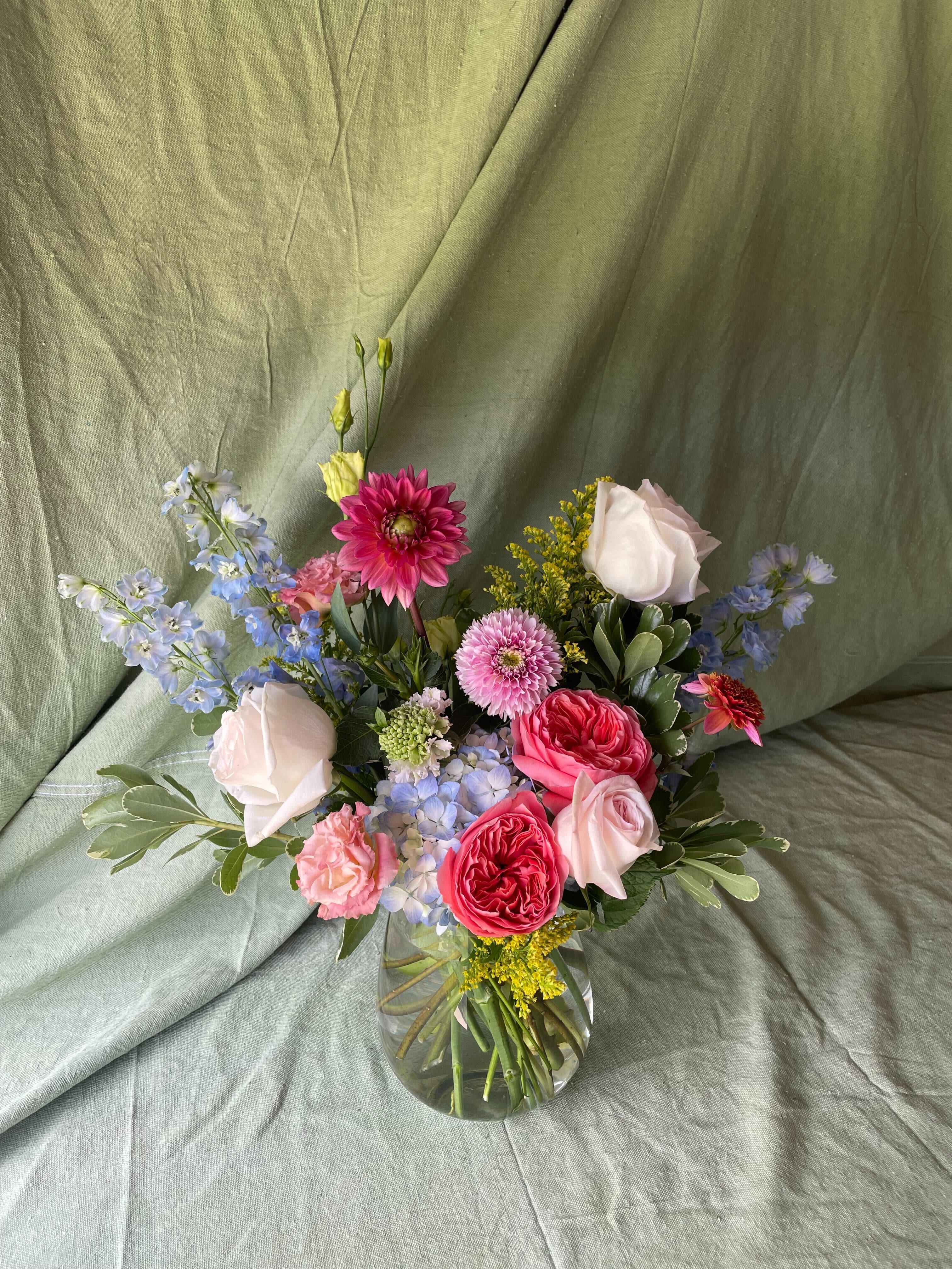 Classic-Florist's Choice - Indulge in the beauty of our Classic arrangement, a luxurious bouquet brimming with premium textures and blooms. Each arrangement is a unique creation, thoughtfully crafted with a diverse mix of seasonal flowers, lush greenery, and elegant accents. The arrangement will vary each week, ensuring that you receive a fresh and personalized display that reflects the beauty of the season. Perfect for adding sophistication and charm to any space, this garden-inspired arrangement is an exquisite way to celebrate any occasion or simply elevate your home with nature's finest.    
