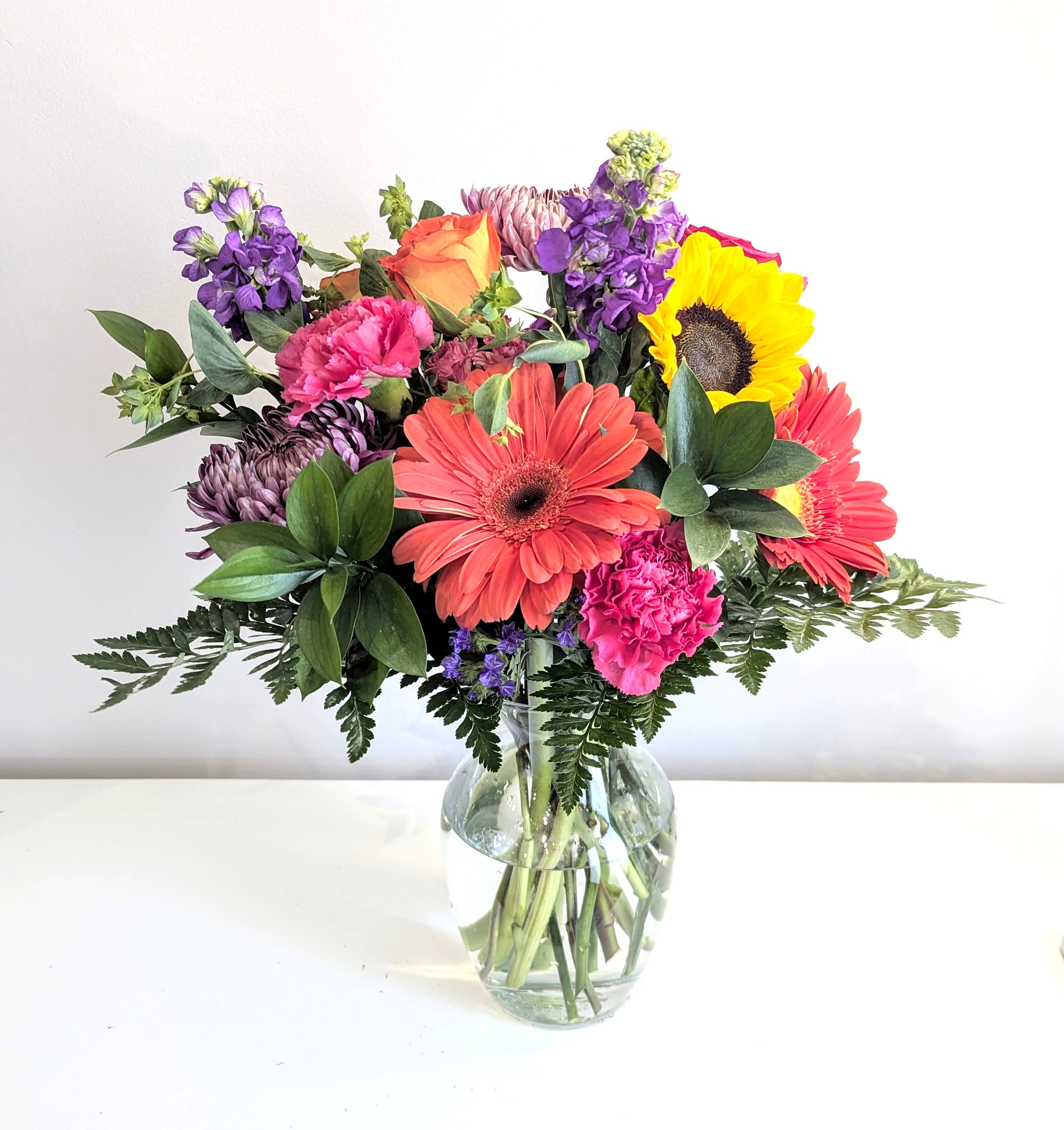 Fruit Punch Fruit Punch - A deliciously, colorful bouquet with hot pink, orange, purple, yellow & green. Roses, sweet smelling stock, gerbera daisies, sunflower, carnations, chrysanthemums & greenery are arranged & delivered in a clear glass rose vase. It's the perfect floral gift for Birthdays, Get Well & other special celebrations. Measures approx. 18" tall & 15" wide Orientation: All around