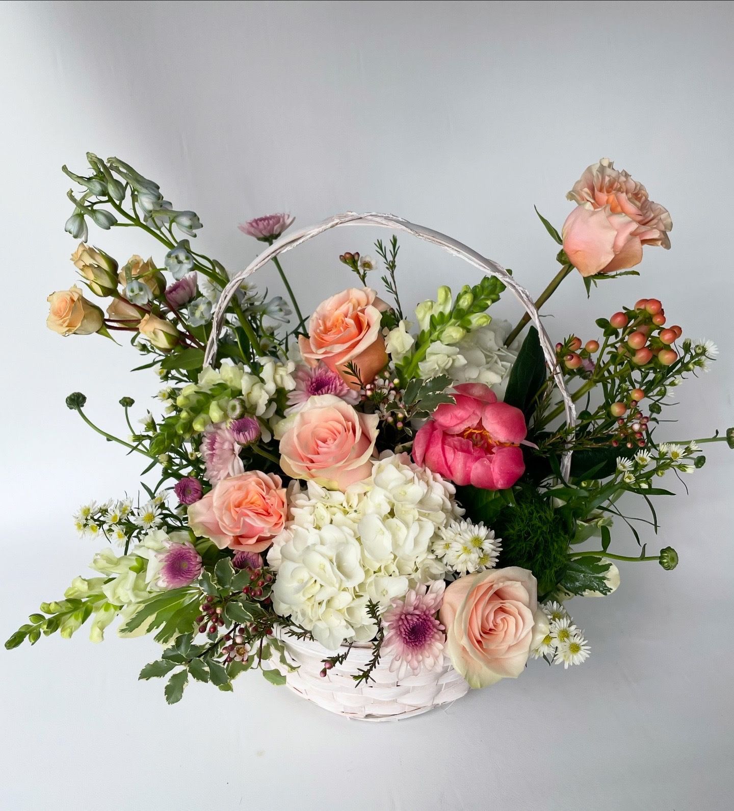 Bloom Basket - A timeless expression of grace and beauty, our Bloom Basket is a thoughtfully arranged floral display presented in a classic wicker basket. Designed with a nod to traditional floral artistry, each arrangement features a curated selection of seasonal blooms that vary weekly based on freshness and availability, ensuring every basket is as unique as the sentiment behind it.  Ideal as a heartfelt gesture for a funeral or memorial service, or as a comforting gift for someone who appreciates classic floral design, the Bloom Basket conveys warmth, remembrance, and enduring elegance.  Please note: Flower varieties and color palettes will vary based on seasonal availability. Each arrangement is hand-designed with care to reflect the freshest flowers on hand.