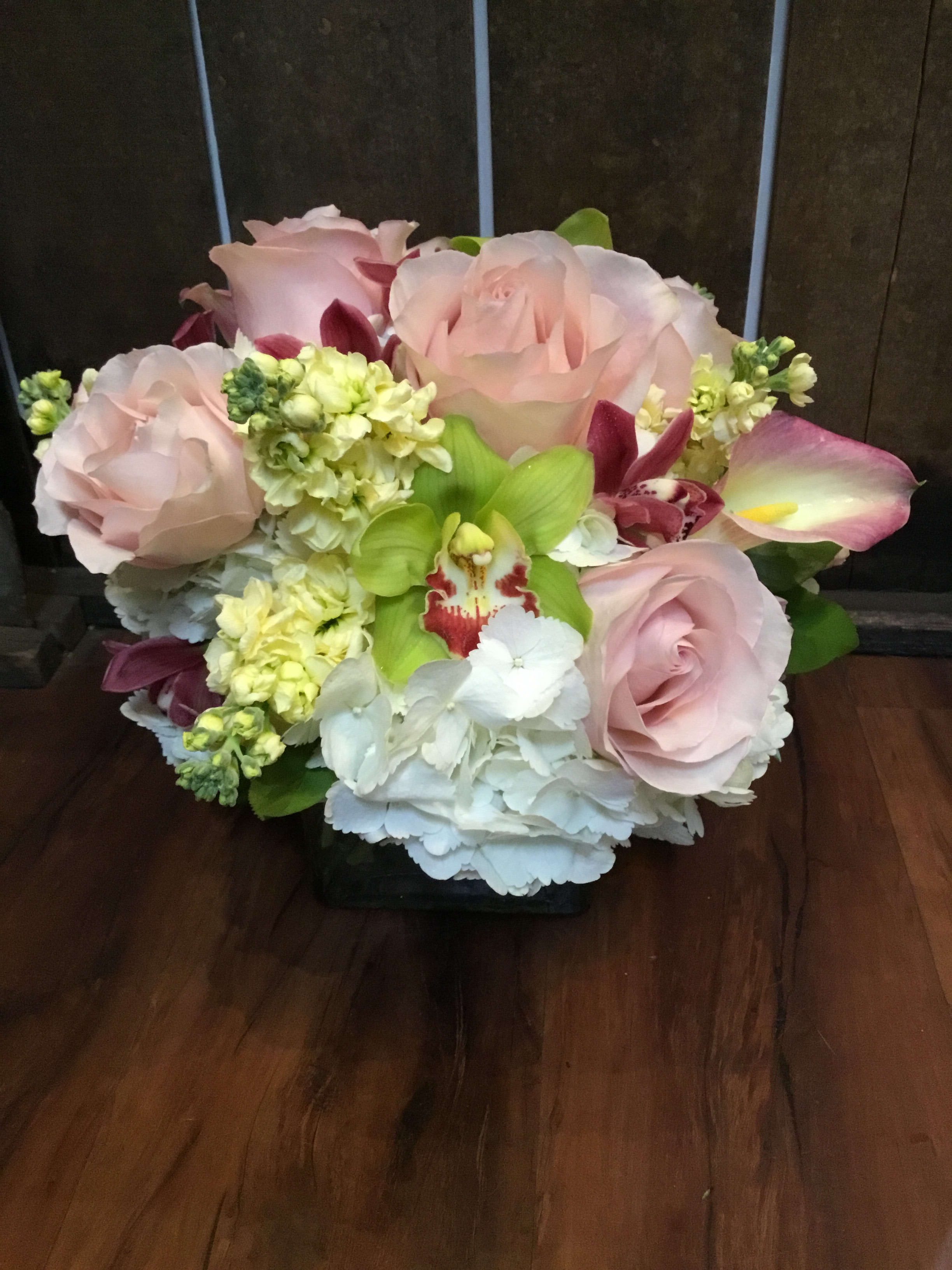 Blushing Elegance - This design is a combination of seasonal callas, hydrangea, roses, stock, and cymbidium orchids. The ideal height for a center piece, side table, or kitchen.