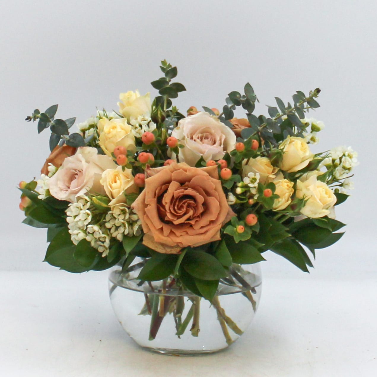 Nudist - Nudist is a fun neutral design featuring gorgeous Toffee Garden Roses, Quicksand Roses, Peach Spray Roses, Peach Hypericum Berries, White Waxflower, Eucalyptus and Israeli Ruscus in a clear glass bubble bowl vase. The Standard and Deluxe Nudist are arranged in six inch bubble bowl vases and the Premium Nudist is designed in an 8 inch bubble bowl vase.