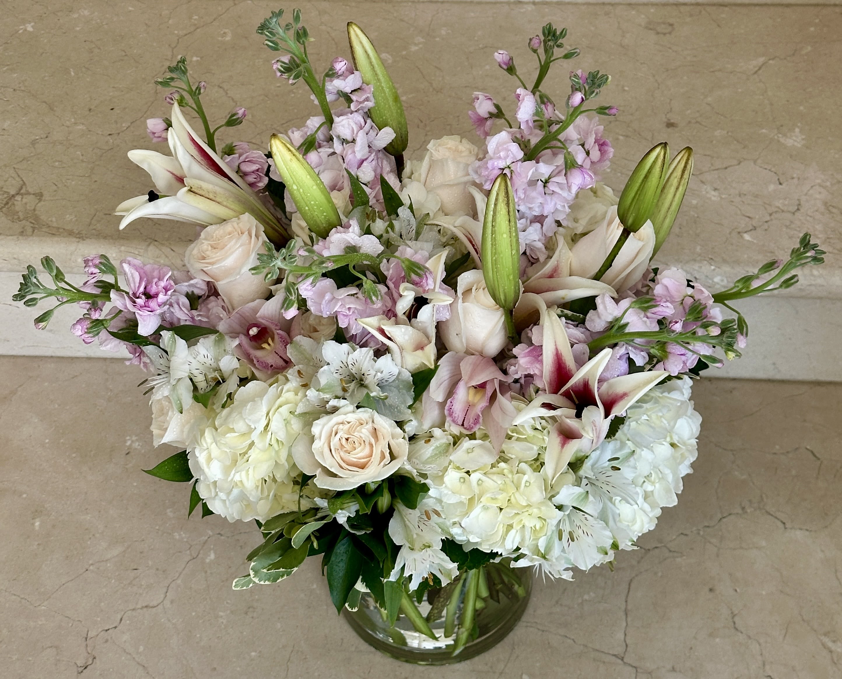 Elegant Pink and White Garden - A lush and romantic mix of soft blush roses, white hydrangeas, star lilies, alstroemeria, and pastel stock—designed in a clear glass vase. This arrangement blends classic beauty with fresh elegance, perfect for expressing love, gratitude, or simply brightening someone’s day.
