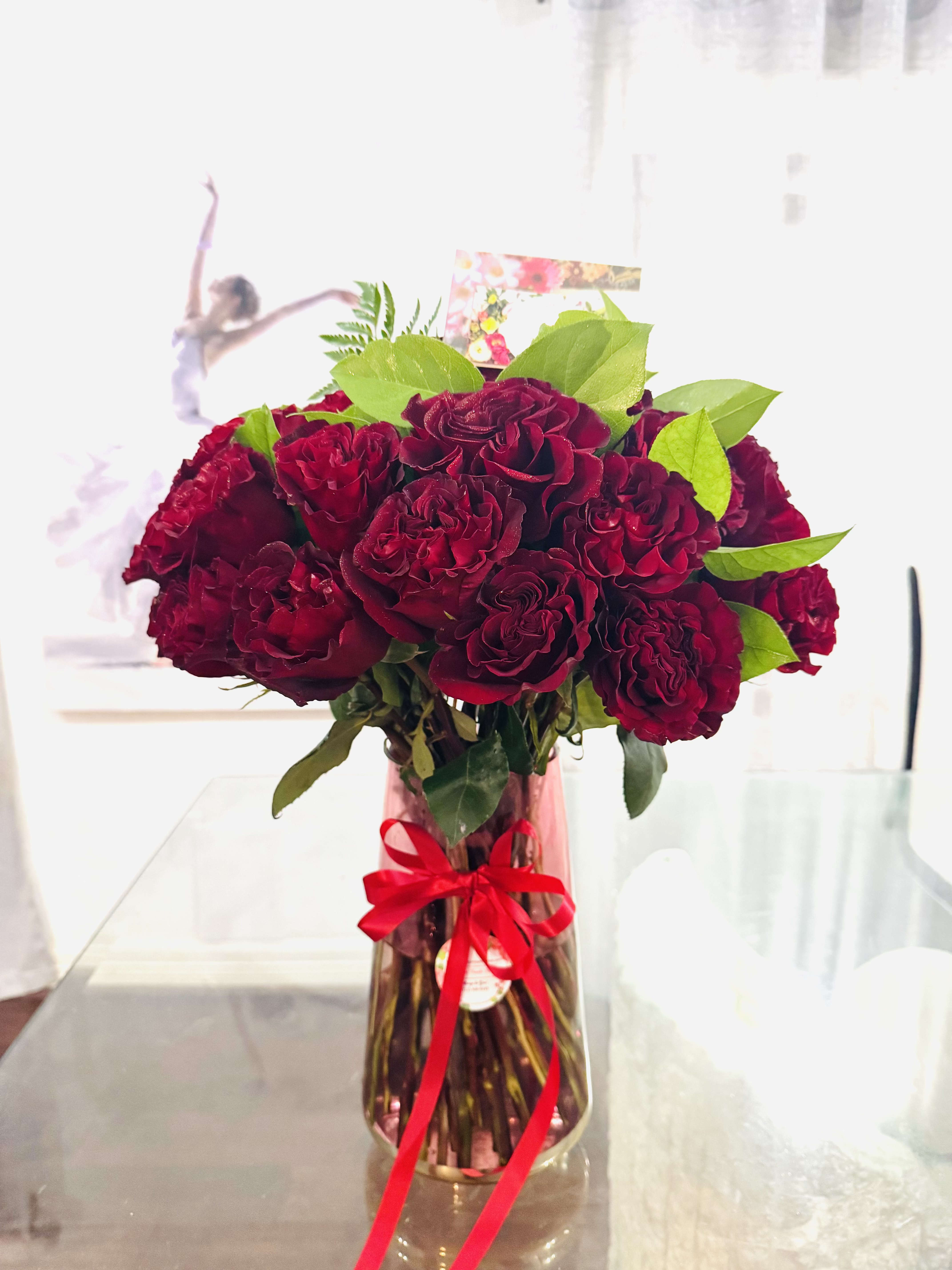 Red Roses - Red Roses in beautiful vase. A radiant arrangement of red roses graces a beautiful vase, exuding timeless elegance and passionate charm. Each rose, with its velvety crimson petals unfurling in perfect symmetry, speaks the language of love and devotion. The bouquet is accented with lush greenery. The vase itself shimmers in the light, elevating the blooms and creating a stunning centerpiece that captures the heart and soul with every glance. Romantic, regal, and endlessly classic. 1 Dozen- Standard (12 Roses) 2 Dozen- Deluxe 3 Dozen- Premium