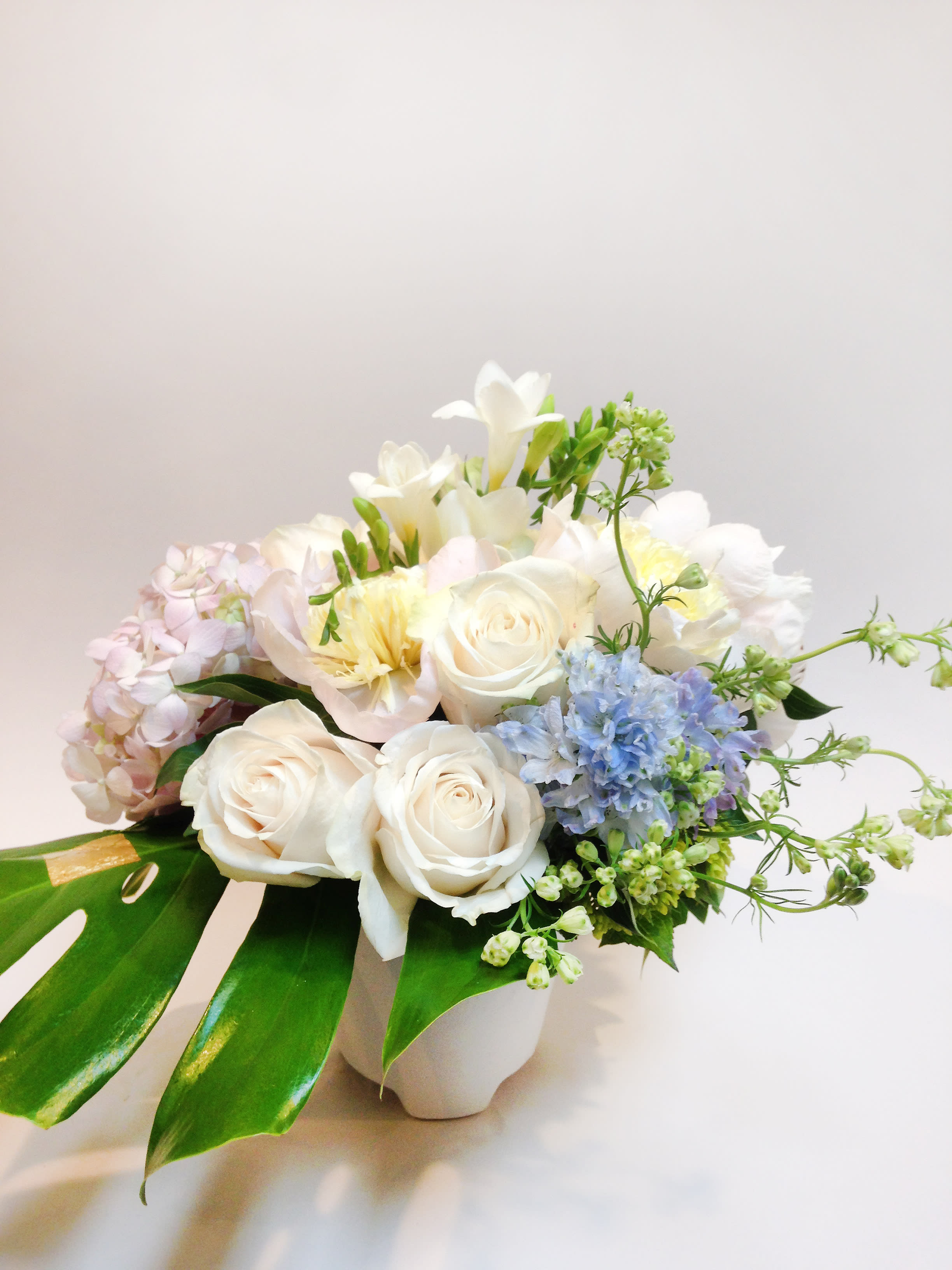 Summer Dance - A classic combination of pastel colors. Comprised of pastel pink peonies, ivory cream roses, pastel blue larkspurs, pink candy hydrangeas, mini green rose spray, mini mojito hydrangeas, fragrant white freesias and green monstera leaf.  Size: 12&quot;w x 8&quot;d x 10&quot;h