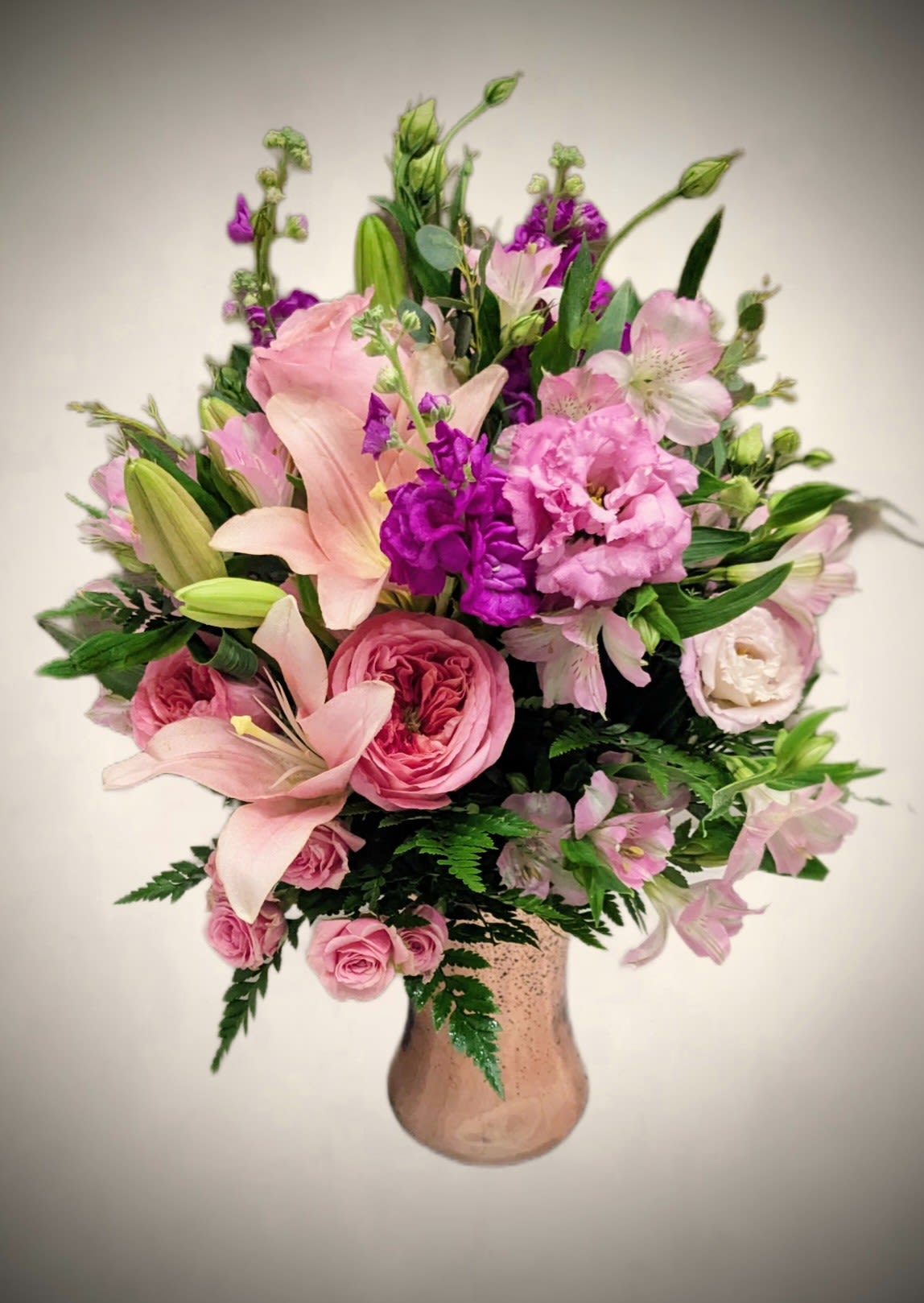 Radiant Romance Radiant Romance - Bursting with charm and color, our Radiant Romance Vase is a joyful celebration of beauty. Soft blush lilies mingle with garden roses, spray roses, and ruffled lisianthus in shades of pink, accented by rich pops of magenta stock and airy alstroemeria. Fresh greenery adds a lush backdrop, while the shimmering rose-gold vase brings a touch of modern elegance. This arrangement is perfect for birthdays, anniversaries, or any moment that calls for something truly unforgettable. Perfect for: Romantic gestures, birthdays, special celebrations Approximate size: 18" H x 14" W