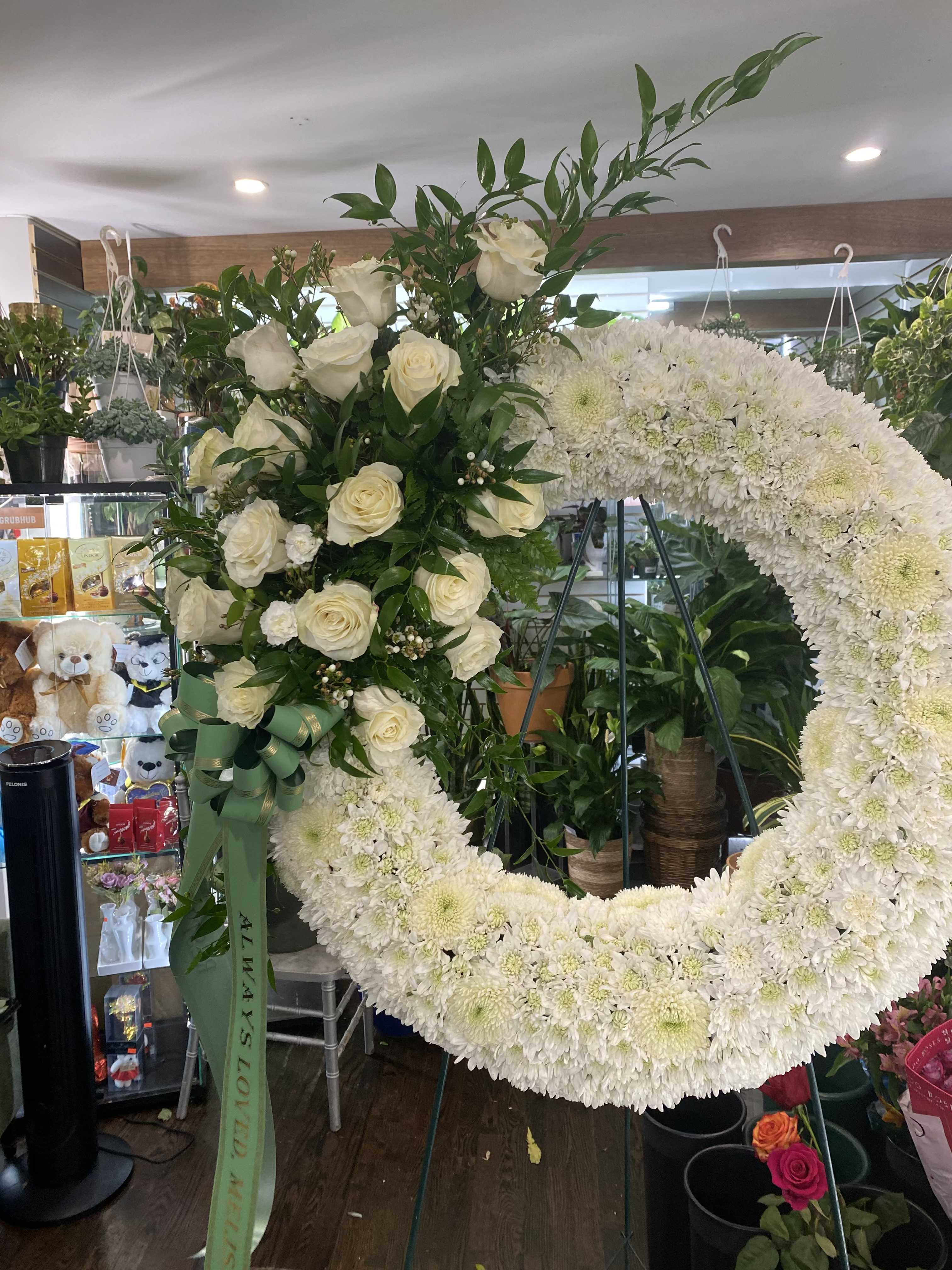Bleeding Wreath in White - This funeral arrangement reinterprets our bleeding wreath arrangement with a serene and ethereal palette, instead focusing on the purity of remembrance, and the delicate nature of loss. This wreath consists of pom pom, long stemmed roses, orchids, and more.