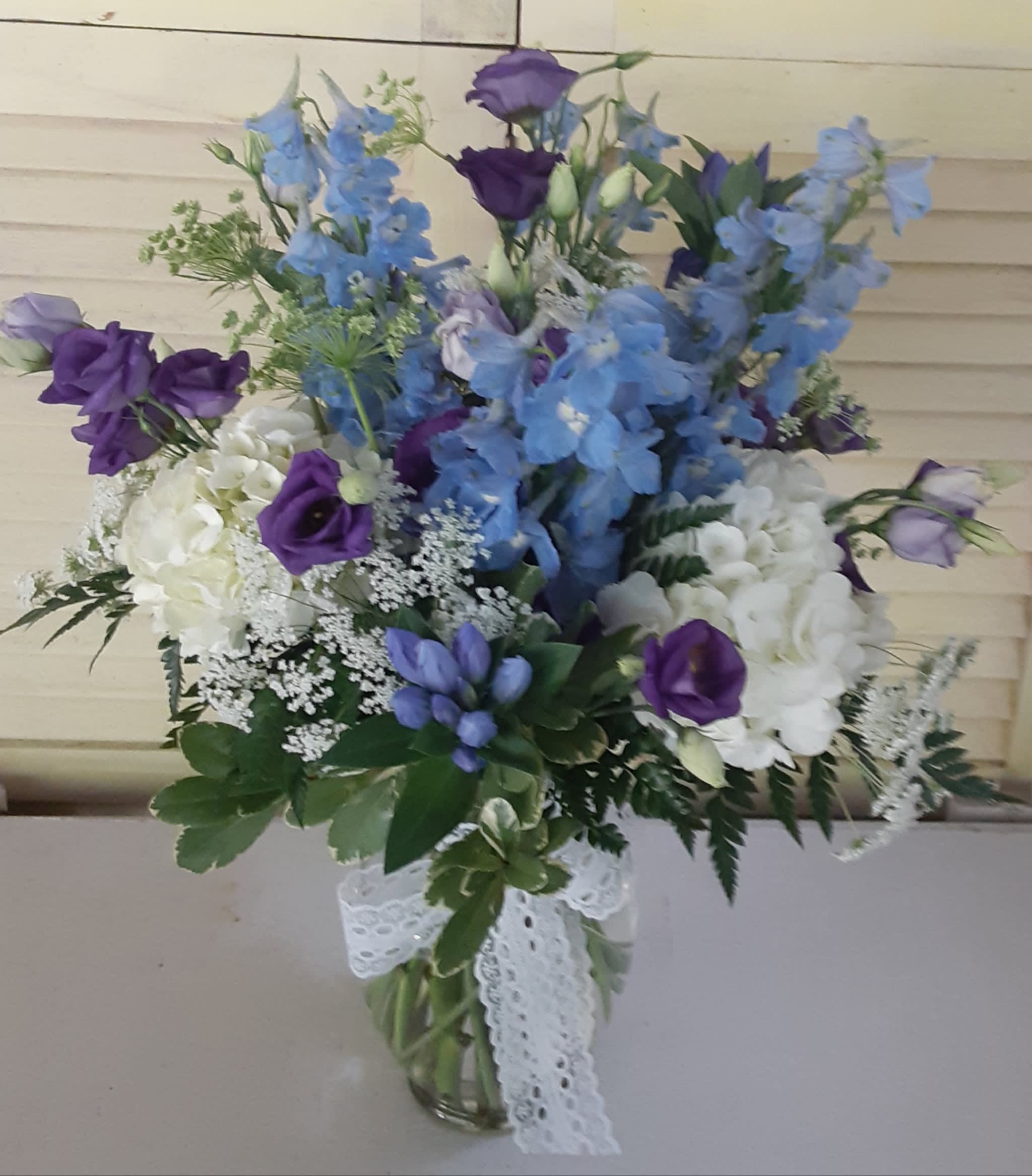 Blue and purple mixed bouquet in a glass vase with a lace ribbon