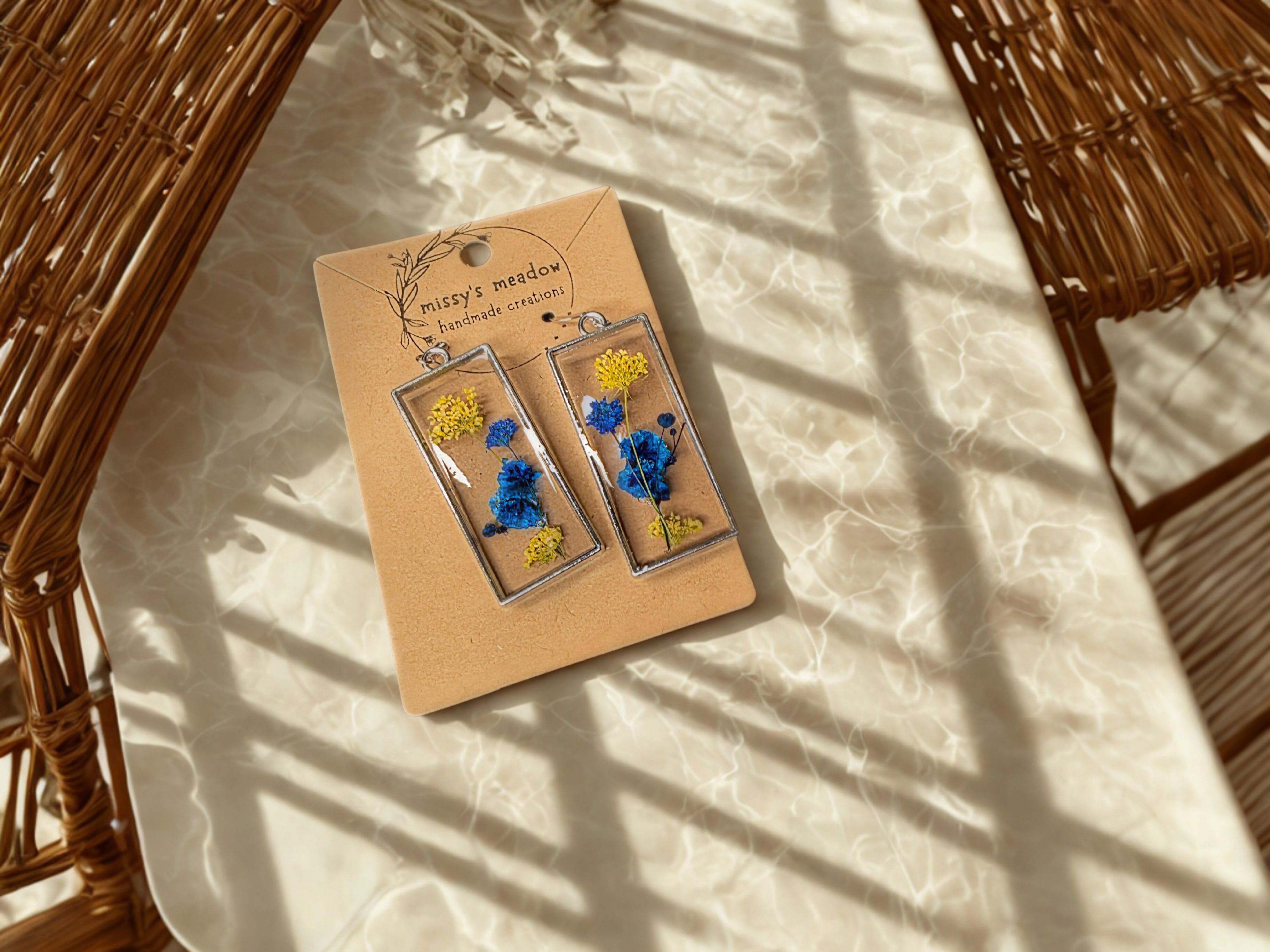 RESIN TEAL FLORALS RESIN TEAL FLORALS - Featuring teal blooms preserved in clear resin, these lightweight, nature-inspired earrings add a graceful pop of color to any outfit.
