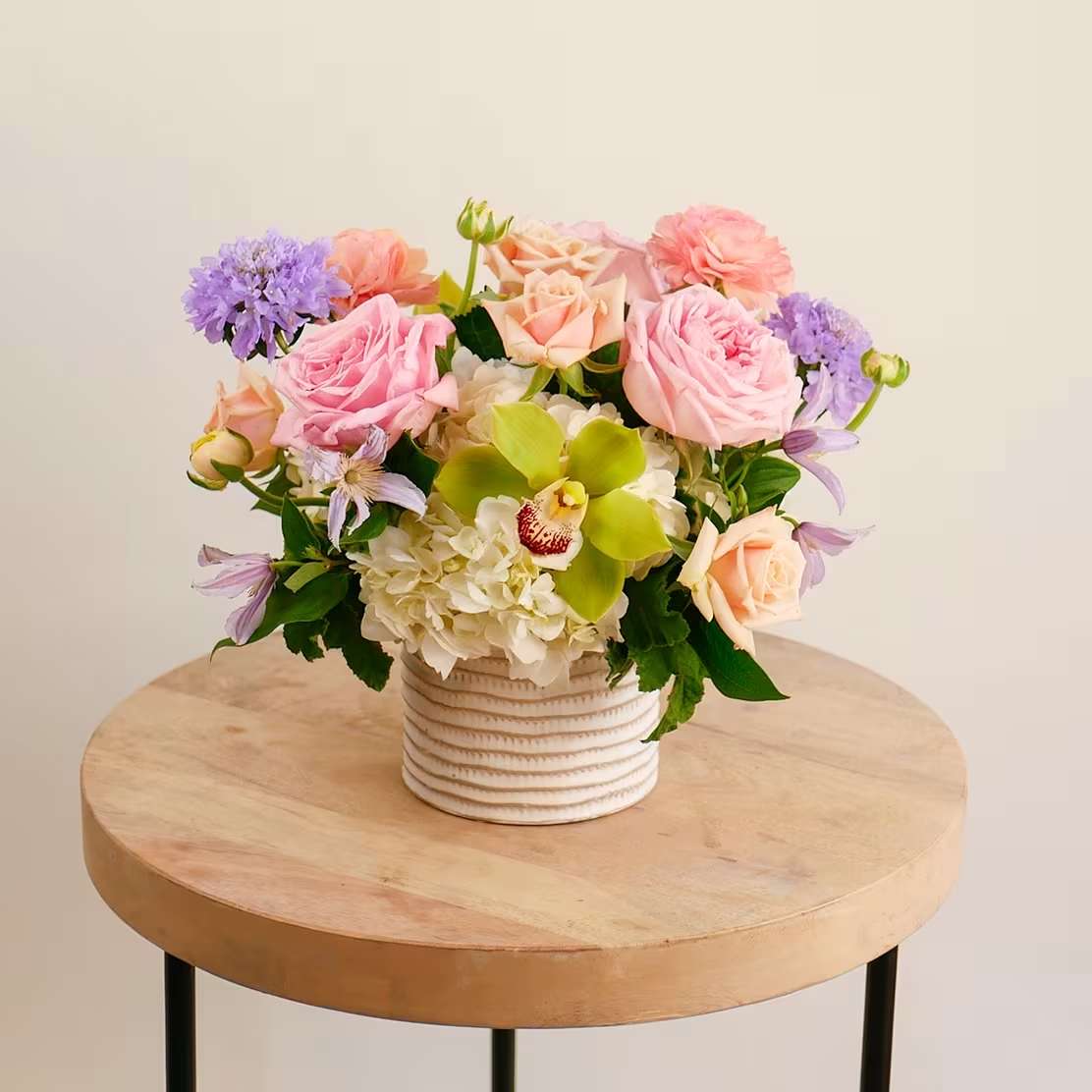 Serendipity - This flower arrangement features soft pastel-toned flowers, including fragrant Pink O'Hara garden roses, ranunculus, lavender scabiosa, clematis, premium white hydrangea and a striking green cymbidium orchid.  We've elevated the classic soft design style by offering the exquisite Pink O'Hara garden roses. Known for their sumptuous, layered petals, delightful fragrance, and impressive longevity, these premium blooms add a touch of luxury to this design.