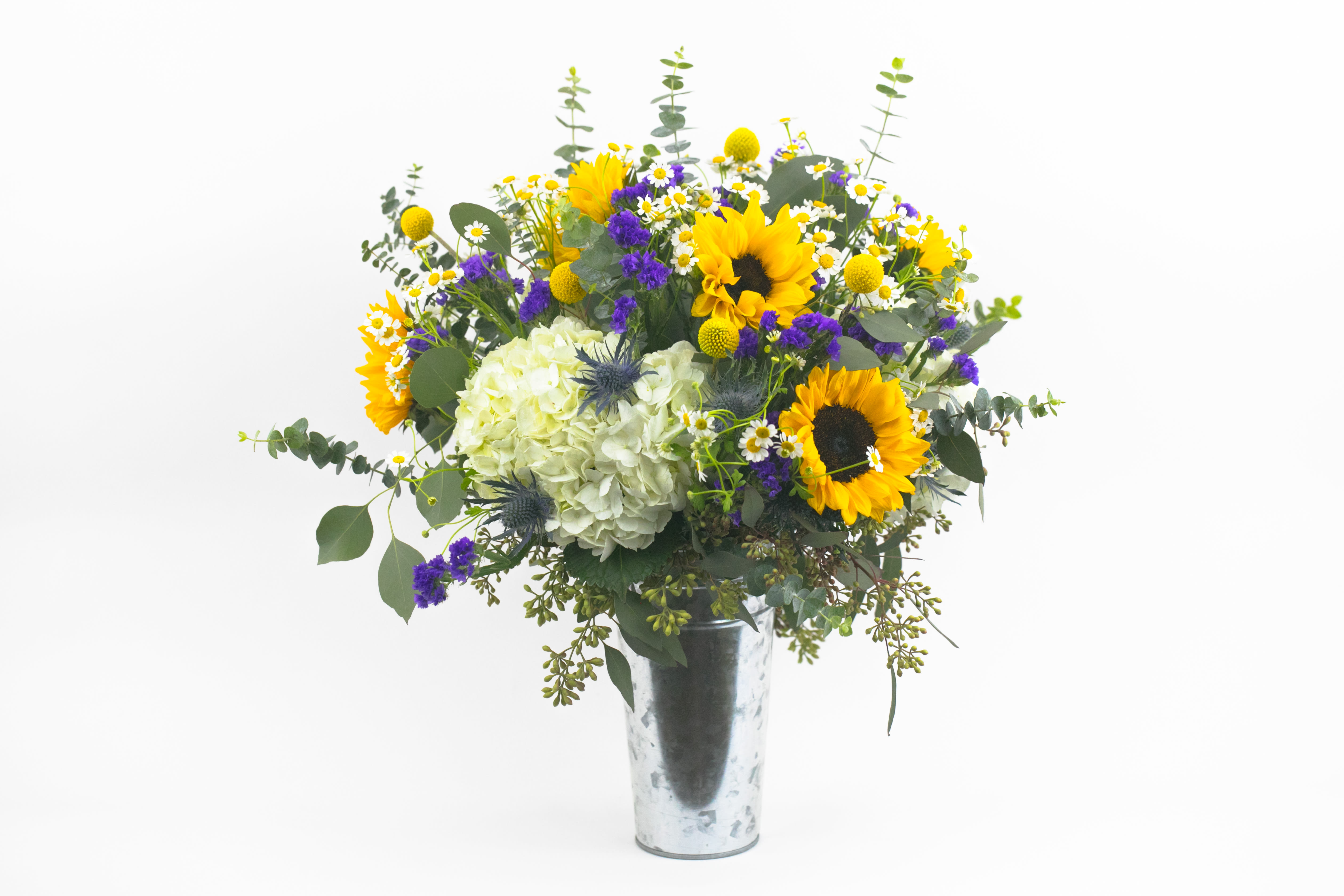 Sunflower Style  - STYLISH VASE OF SUNFLOWERS DELIVERED  Bright and elegant. A gorgeous yellow sunflower arrangement with accents of purple, white and silver. Designed in a galvanized bucket, this classic design features an abundant mass of flowers and foliage. Cheery sunflowers and elegant white hydrangea are the star of the show, while interesting sprigs of silver-blue thistle, dainty white chamomile and curious yellow balls of ‘Billy Buttons’ add interest and texture.  These flowers are perfect for people who adore sunflowers and appreciate traditional, classic styles.  Send this beautiful sunflower arrangement to celebrate the birth of a new baby or wish someone a special happy birthday or get well soon. Deliver to a client or colleague in recognition of an achievement or as a thank you. This design is perfect for all occasions.  Why not add a greeting card, bunch of local dried lavender or quality handmade candle to match the occasion or personality?  Sunflower Style features: ·        Sunshine yellow sunflowers ·        Fluffy balls of white hydrangea ·        Spiky silver-blue thistle ·        Yellow Craspedia (or ‘Billy Buttons’) ·        Long-lasting purple statice ·        Dainty sprigs of white chamomile ·        Spiral eucalyptus ·        Seeded eucalyptus ·   	Galvanized bucket   SIZE: The STANDARD flower arrangement is approximately 14” height and 14” width.   ALLERGY ADVICE: This design has moderate-high pollen and a low fragrance.   FAQ Q: What time will my flowers arrive and what if no-one is there to accept them? A: Excellent question! We’re unable to provide or guarantee specific delivery times. All our flowers are delivered anytime between 9-5pm, with exception to Sympathy designs for a funeral service. For full details around our delivery process and timings, please see our Terms and Conditions. Q: What days do you deliver flowers? A: All our flowers are available for San Francisco and Daly City delivery seven days a week, between 9am-5pm. Q: May I order for the same day delivery? A: Yes, same day deliveries are available if you place an order before 1pm. Q: May I request to change the design a bit? A: Yes, please make a note in the SPECIAL INSTRUCTION box when you place your online order. We will do our best to follow them. Q: Will my flowers look exactly as what is pictured? A: Depending on the season, colors or shades may vary. Sometimes we need to substitute flowers due to seasonal availability, but they’re always substituted for the same or greater value.   Ready to bring floral beauty into someone’s world with our sunflower delivery? Order this gift online now or give us a call on (415) 752-2060 if you have a question or special request. 