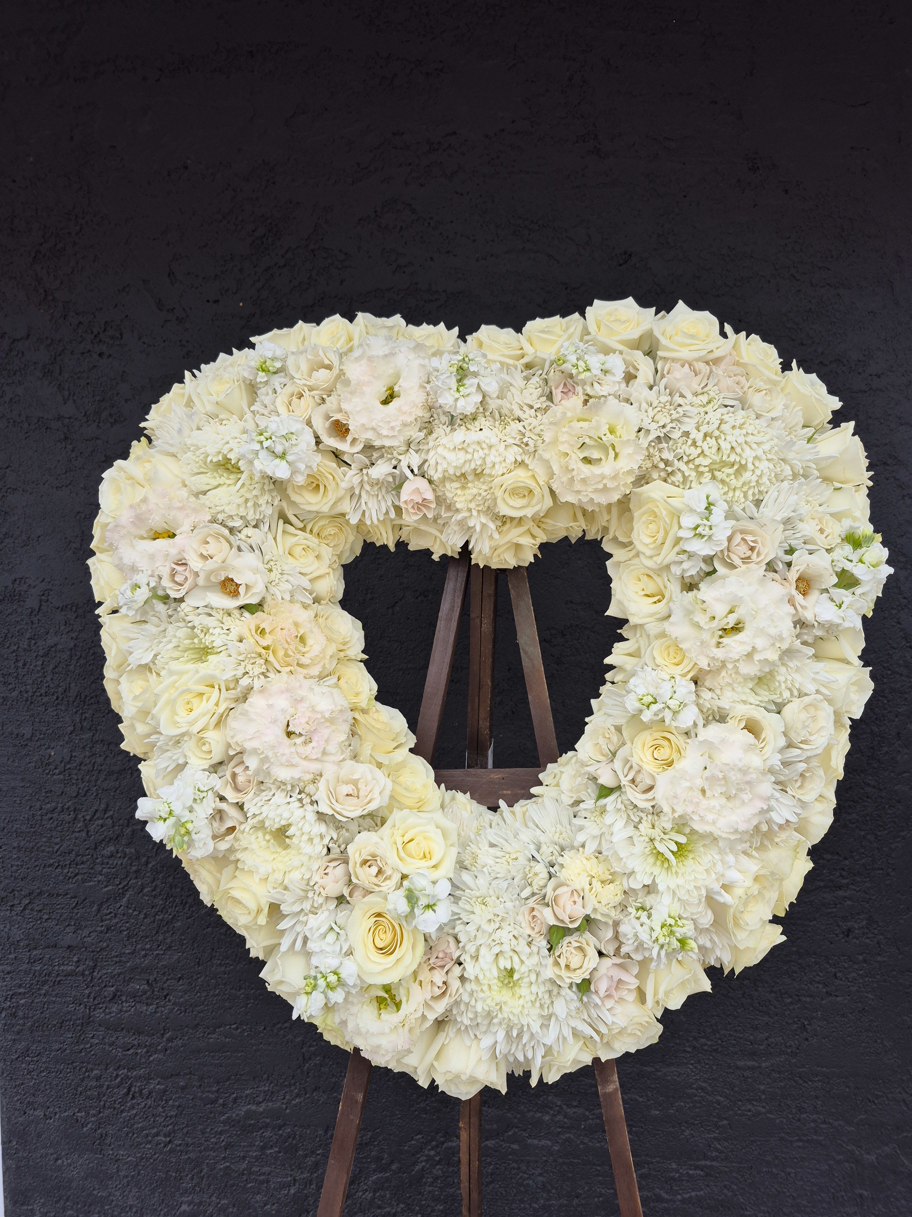 Heavenly Garden Open Heart Wreath - White - • Open, heart-shaped arrangement of all white roses, pomegranate poms, lisianthus, stocks, carnations, and garden roses. • Measures approximately 28&quot;x28&quot; without easel.  • Arrangement is designed on a easel and can be accented with a satin ribbon.  • Appropriate for funeral home. • Our florists use only the freshest flowers available, so colors and varieties may vary depending on the season of availability. 